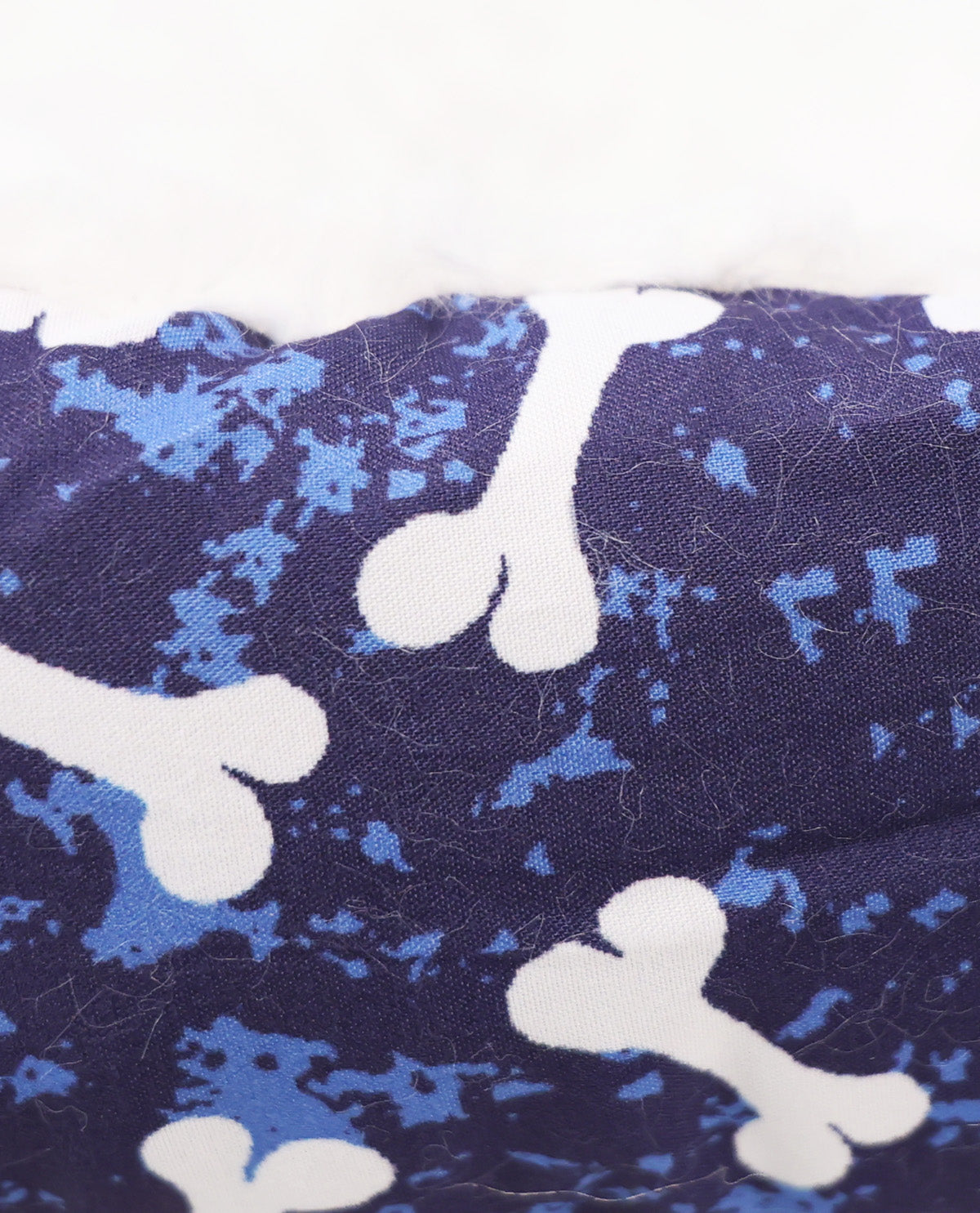 Close-up of a fabric surface with a dark navy background, light blue splatter pattern, and large white bone motifs.