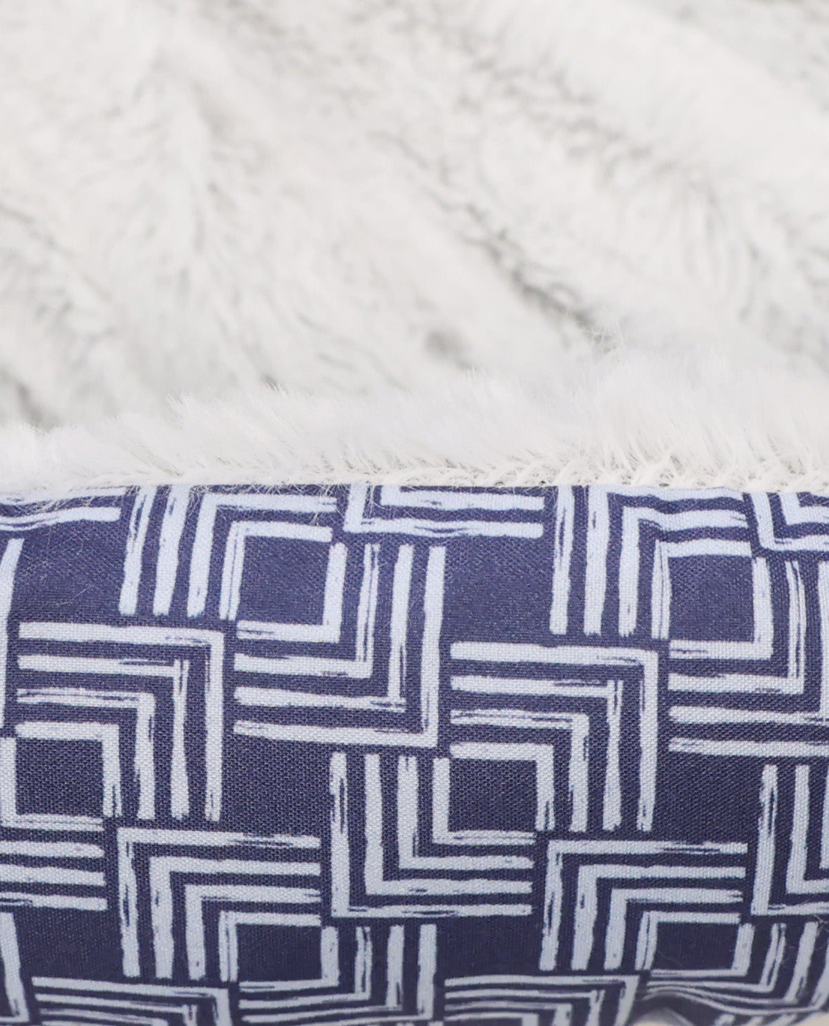 Close-up of a plush throw blanket showing two textures: a soft white faux fur side and a navy blue woven side with a white geometric line pattern.