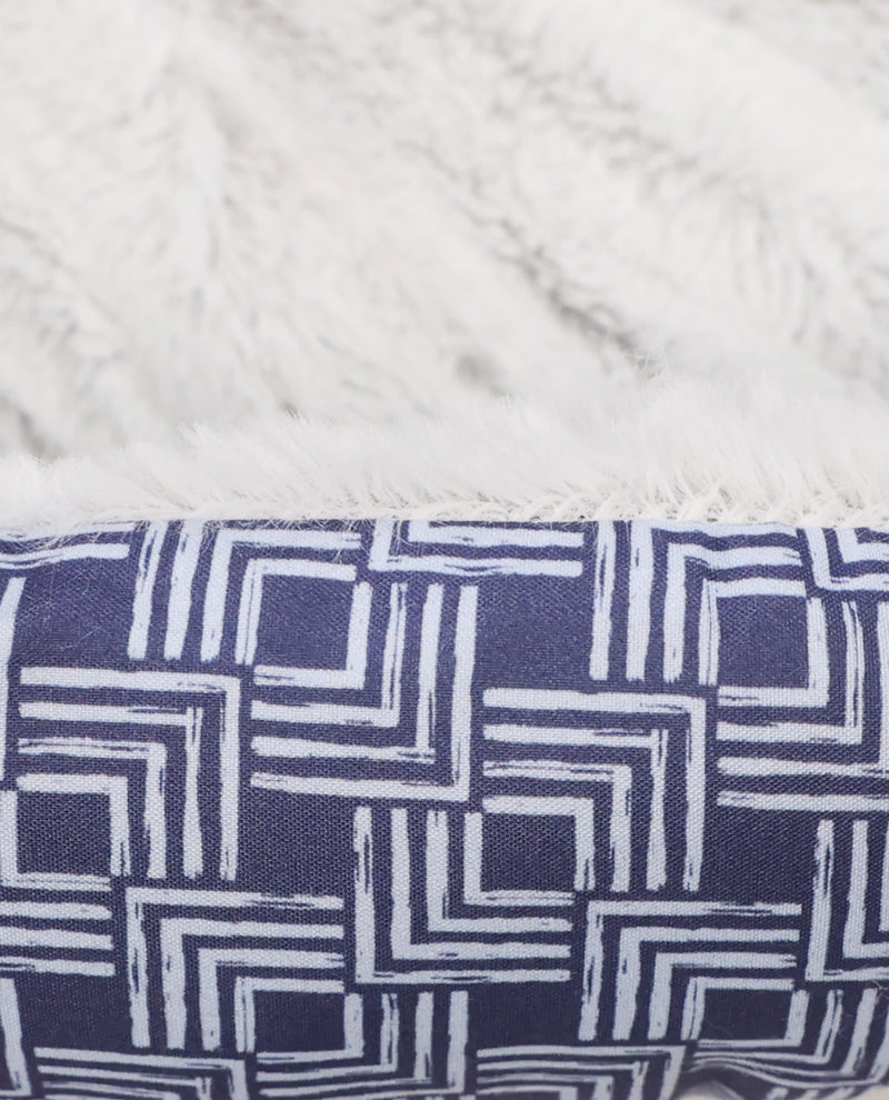 Close-up of a plush throw blanket showing two textures: a soft white faux fur side and a navy blue woven side with a white geometric line pattern.