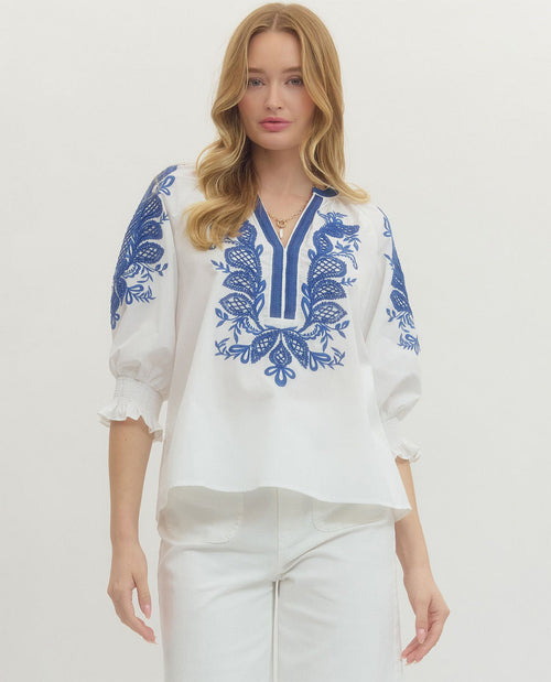 Woman wearing a white blouse with blue embroidery on a plain background