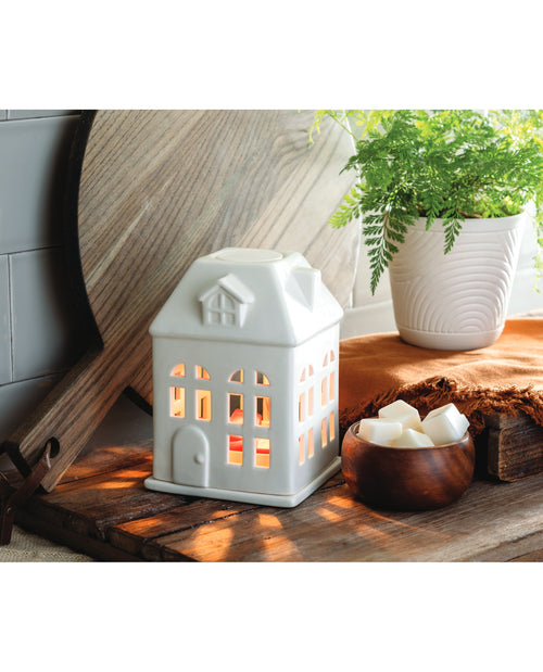 White house-shaped lantern with a wooden surface and plant in the background