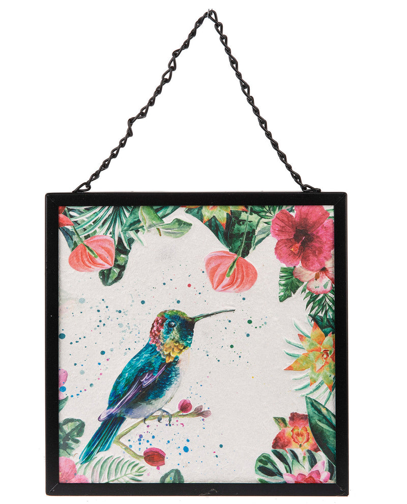 A square framed wall hanging with a black metal frame and hanging chain, featuring a colorful watercolor-style hummingbird surrounded by tropical flowers and leaves on a light background.