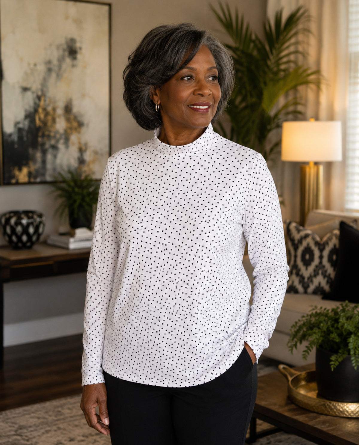 Woman wearing a white blouse with black polka dots in a living room setting.