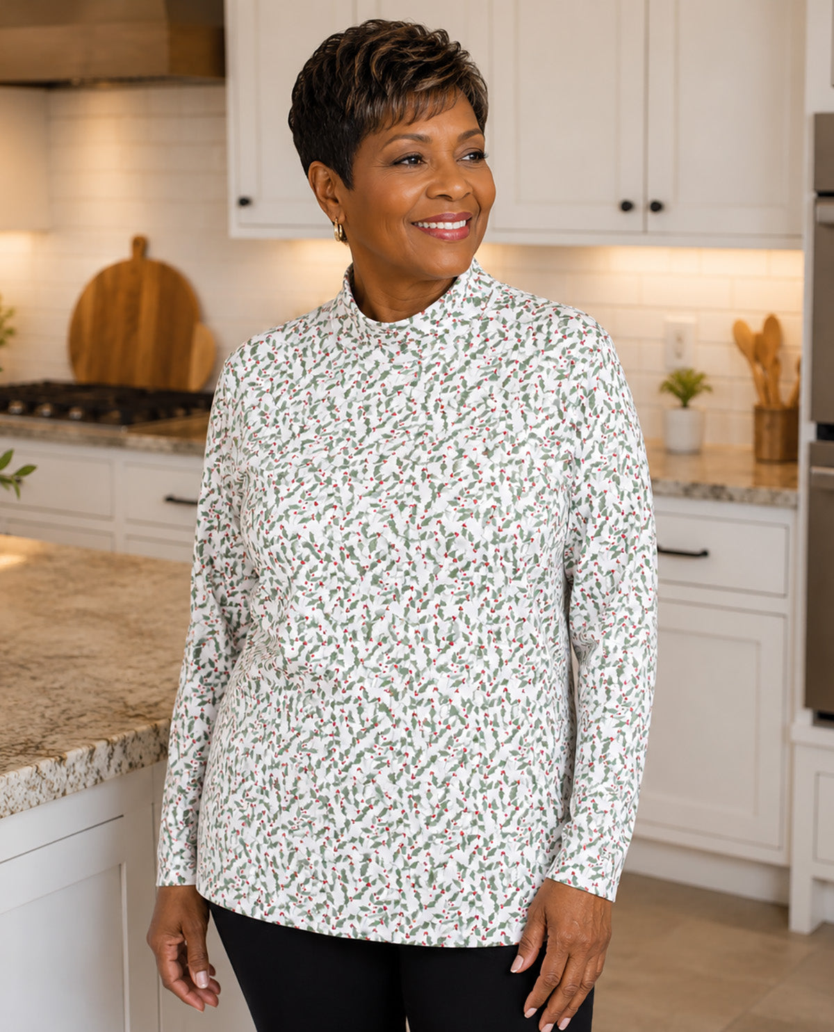 A woman wearing a white long-sleeve mock neck top with a dense small floral print in green, red, and pink, standing in a bright white kitchen.