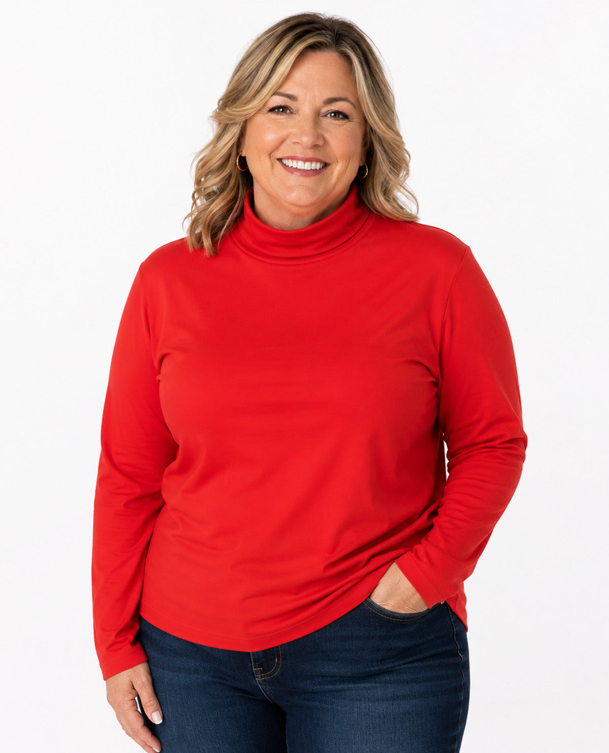 A smiling woman with blonde hair wearing a bright red long-sleeve turtleneck top and dark blue jeans, standing against a plain white studio background.