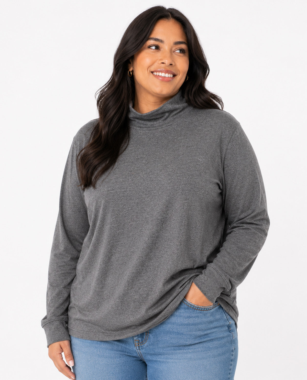 A woman wearing a dark gray heathered long-sleeve turtleneck top and blue jeans, standing against a plain white studio background.