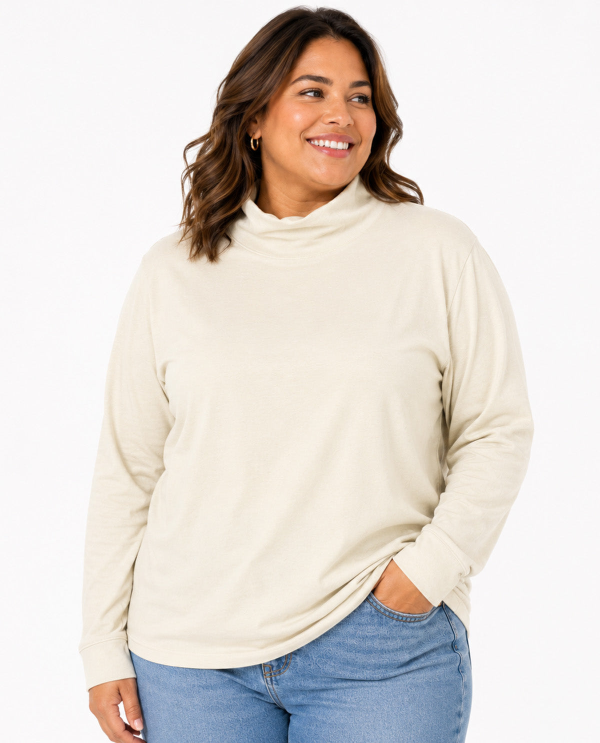 A woman wearing a cream-colored long-sleeve mock neck top and light blue jeans, standing against a plain white background.