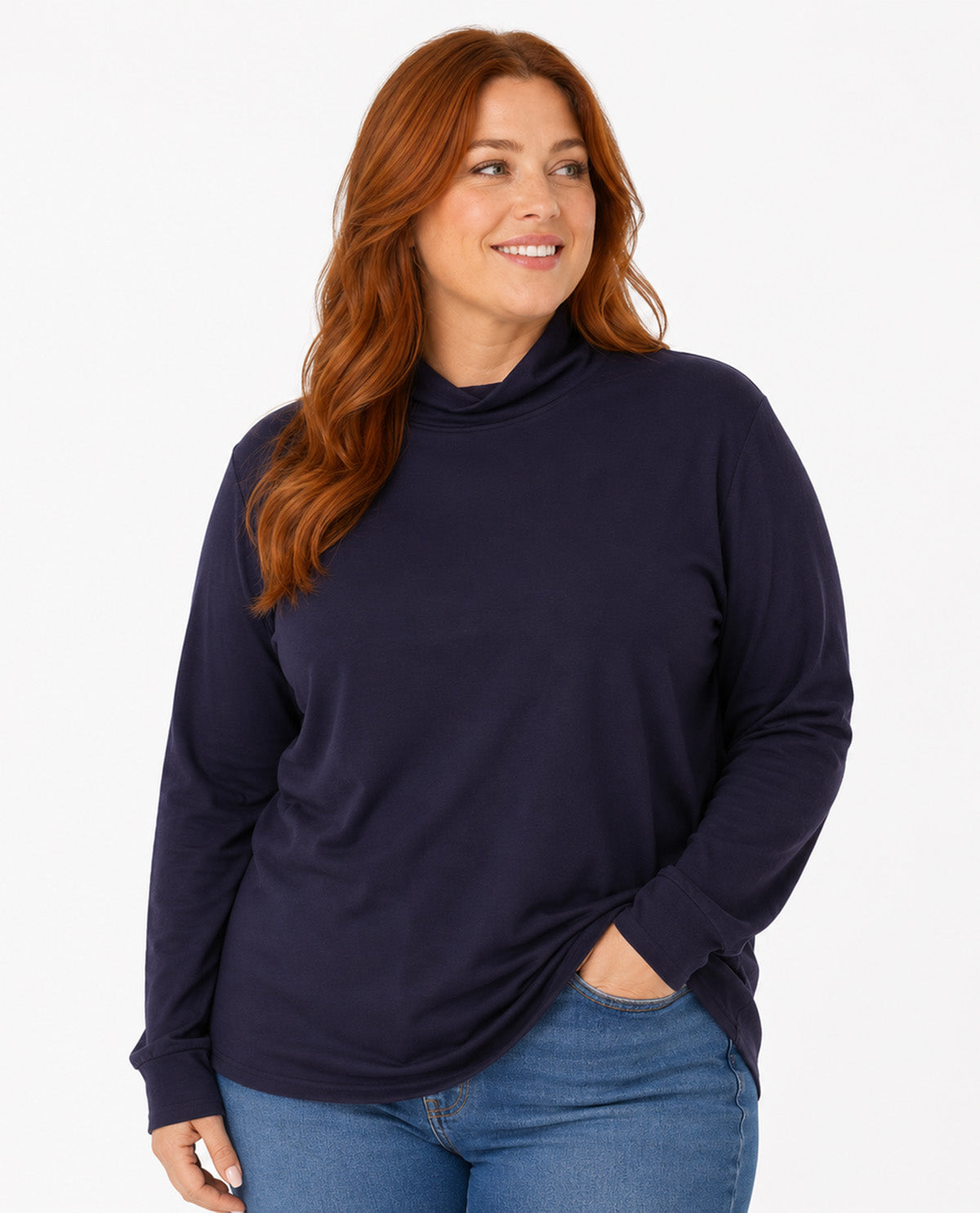 A woman with red hair wearing a dark navy long-sleeve mock neck top and blue jeans, standing against a plain white studio background.