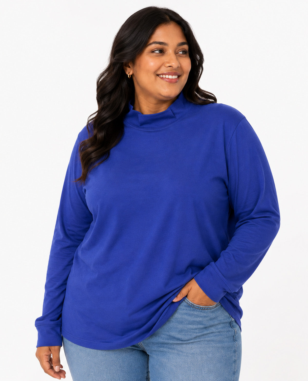 A woman wearing a royal blue long-sleeve mock neck top and light wash blue jeans, standing against a plain white studio background.