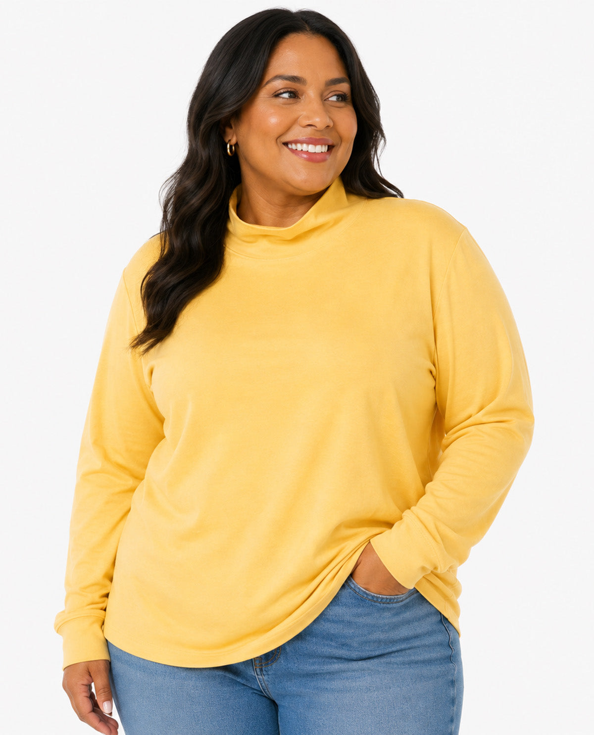 A woman wearing a bright yellow long-sleeve mock neck top and blue jeans, standing against a plain white studio background.