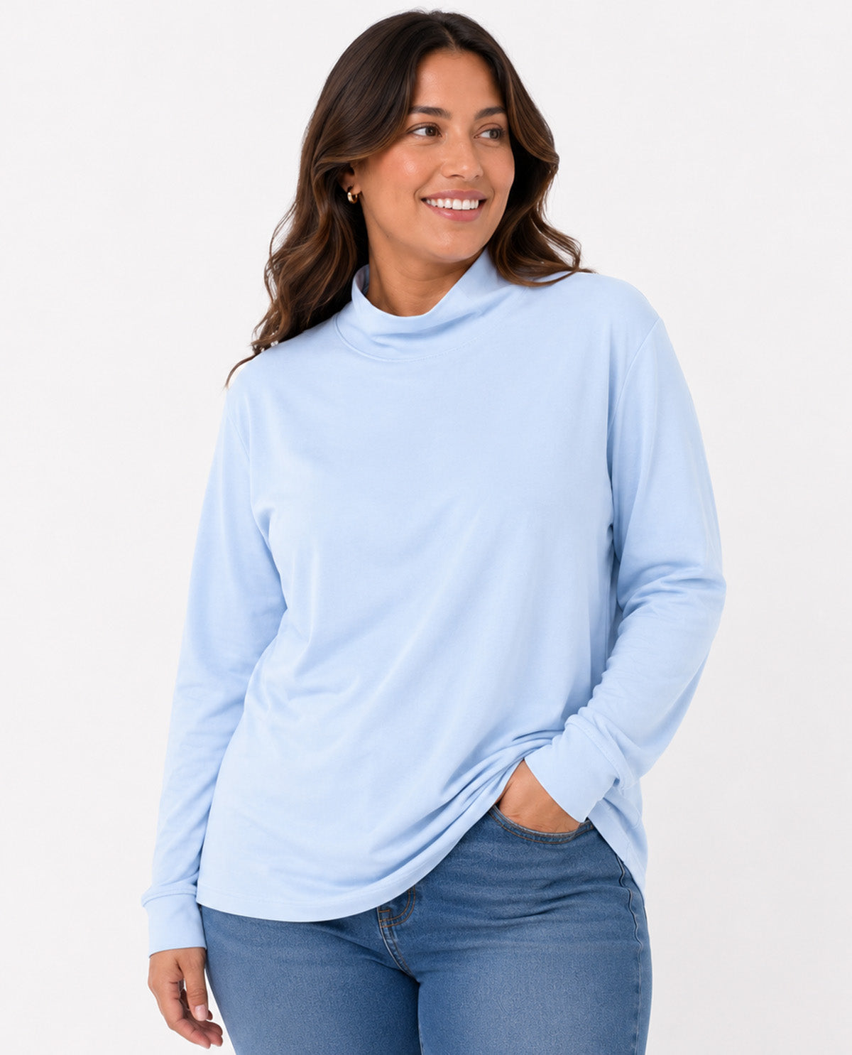 A woman wearing a light blue long-sleeve mock neck top and blue jeans, standing against a plain white studio background.
