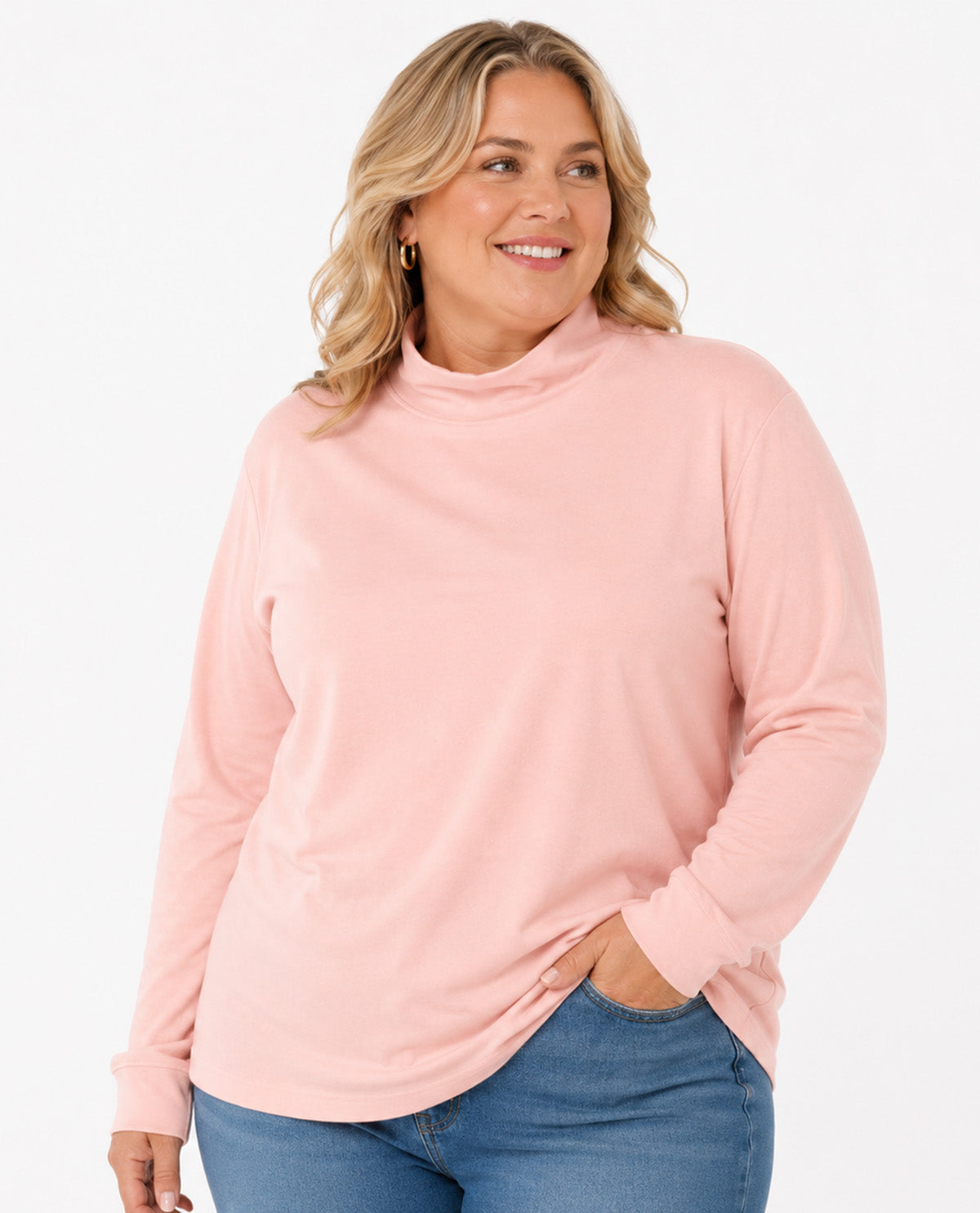 A woman wearing a light pink long-sleeve mock neck top and blue jeans, standing against a plain white studio background.
