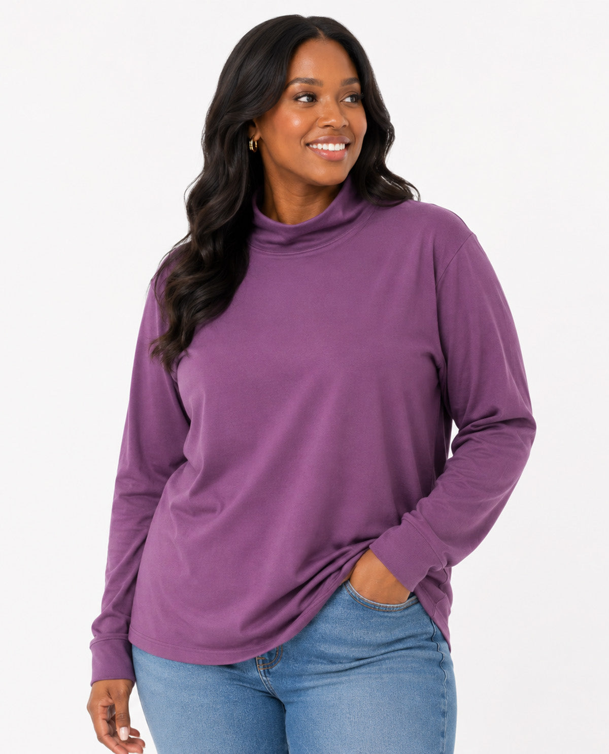 A woman wearing a purple long-sleeve mock neck top and blue jeans, standing against a plain white studio background.