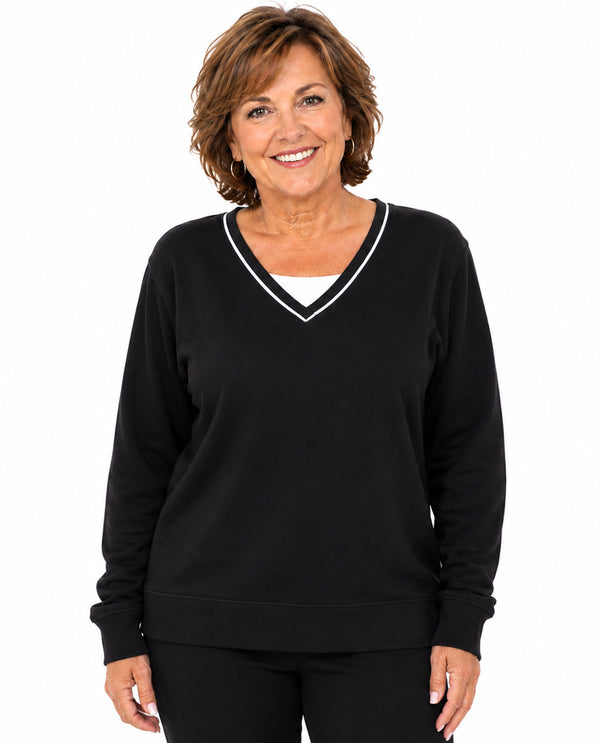 A smiling woman with short brown hair wearing a black long-sleeve V-neck sweatshirt with white trim, layered over a white undershirt, against a plain white background.