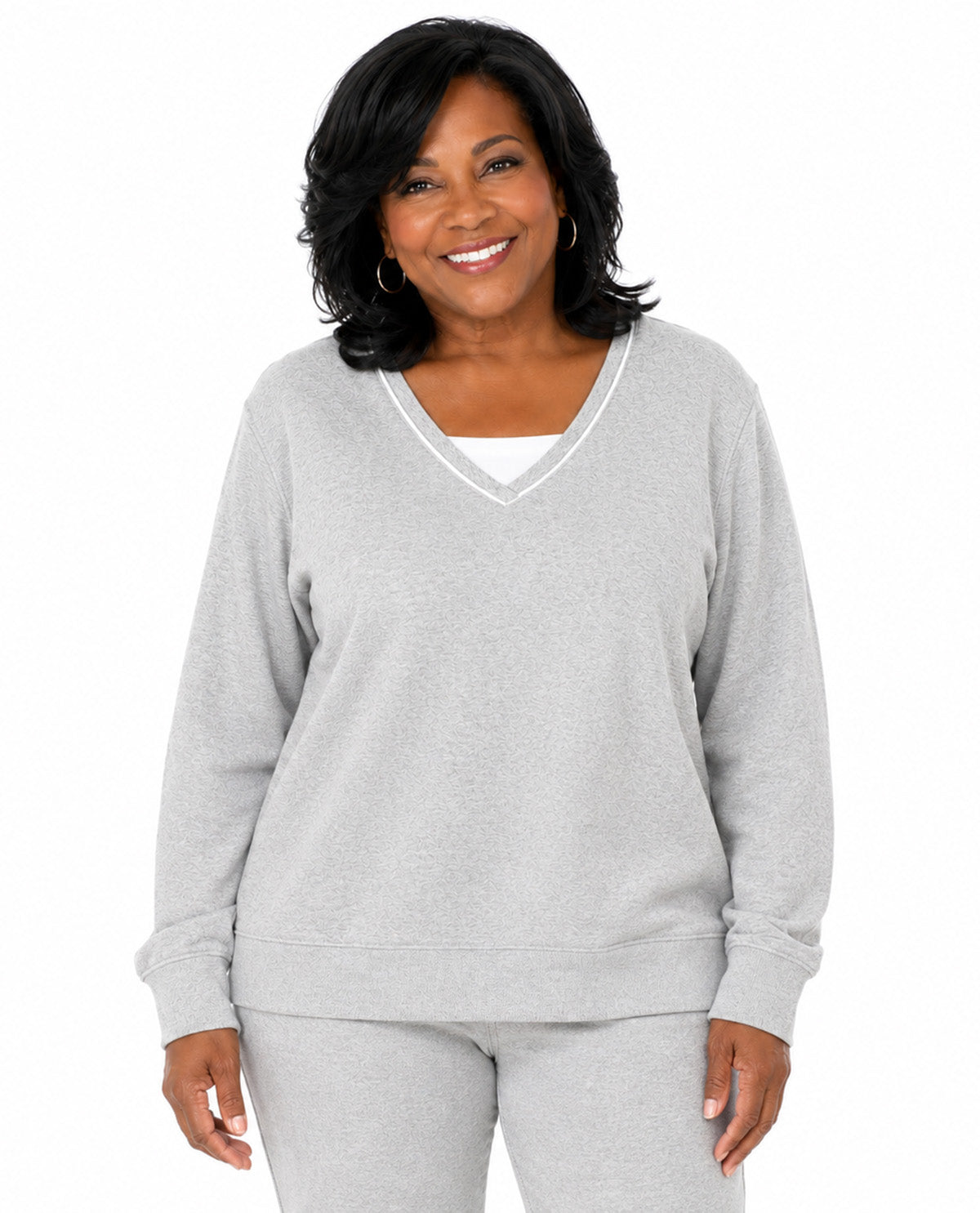A smiling woman with short dark hair models a light gray heathered V-neck sweatshirt and matching sweatpants against a plain white background.