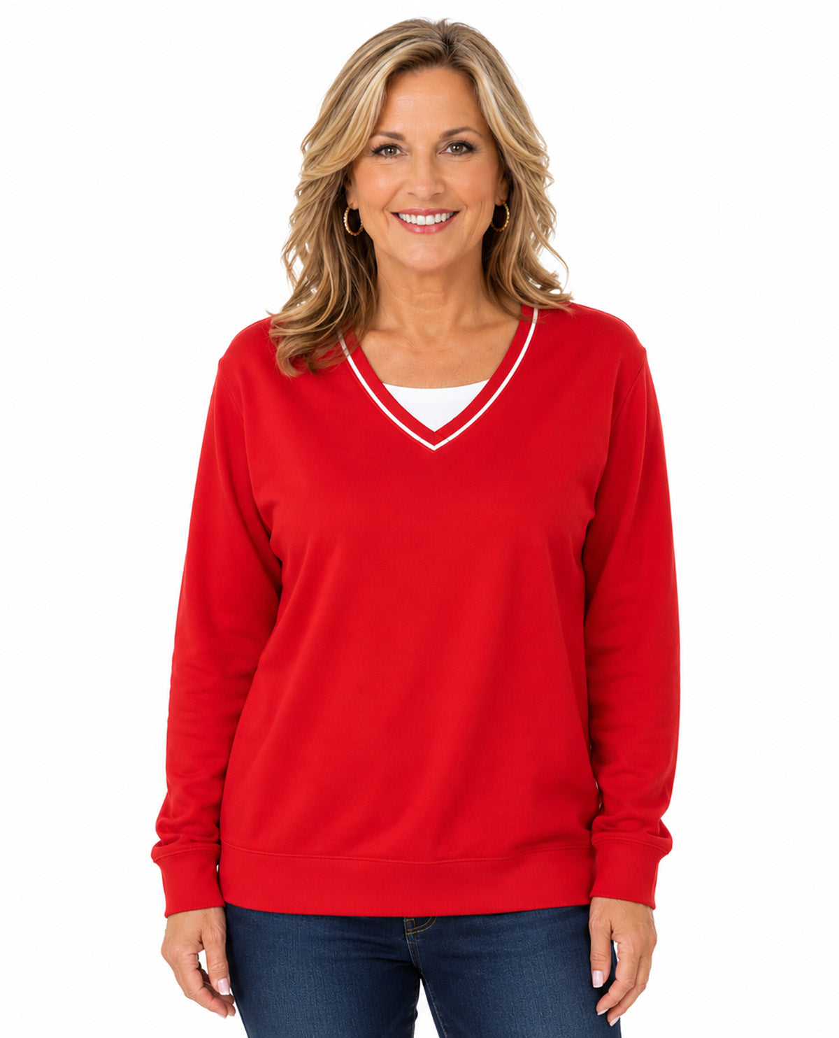 A smiling blonde woman wearing a bright red long-sleeve V-neck sweater with a thin white trim, paired with dark blue jeans, against a plain white background.
