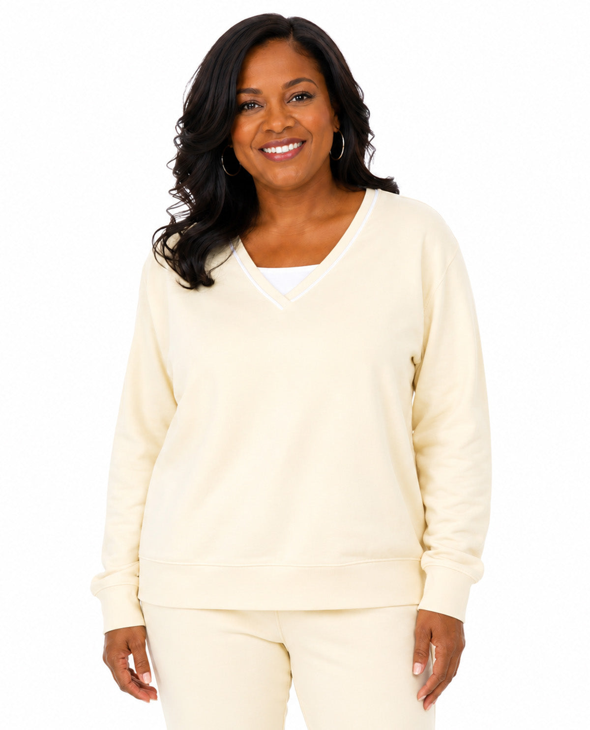 A woman modeling a cream-colored V-neck sweatshirt and matching sweatpants against a plain white background.