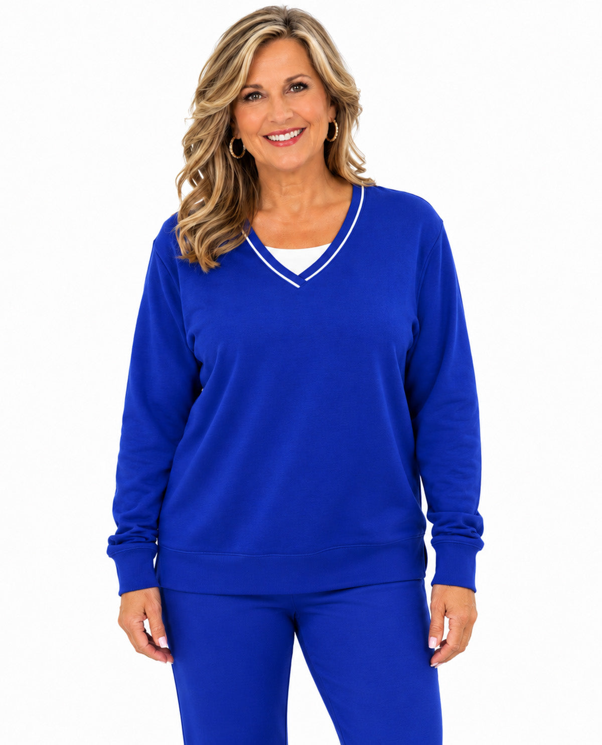 A smiling woman with blonde hair models a royal blue long-sleeve V-neck sweatshirt with white trim, paired with matching blue leggings, against a plain white background.