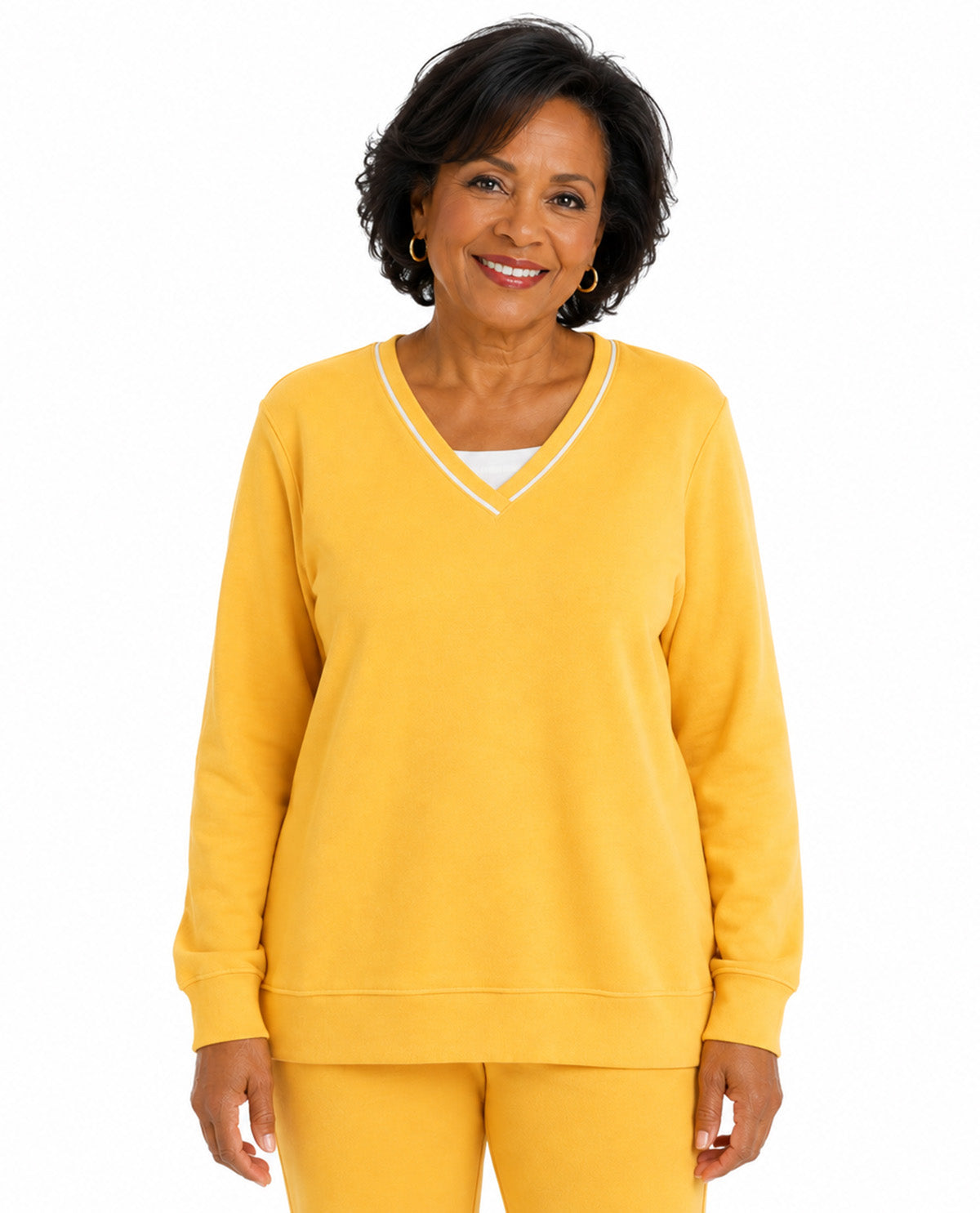 A smiling woman with short dark hair models a yellow V-neck sweatshirt with white trim and matching yellow pants against a plain white background.