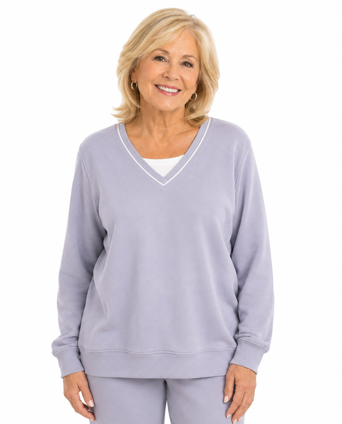 A smiling blonde woman wearing a light lavender-gray V-neck sweatshirt with white piping trim over a white undershirt, paired with matching sweatpants, against a plain white background.
