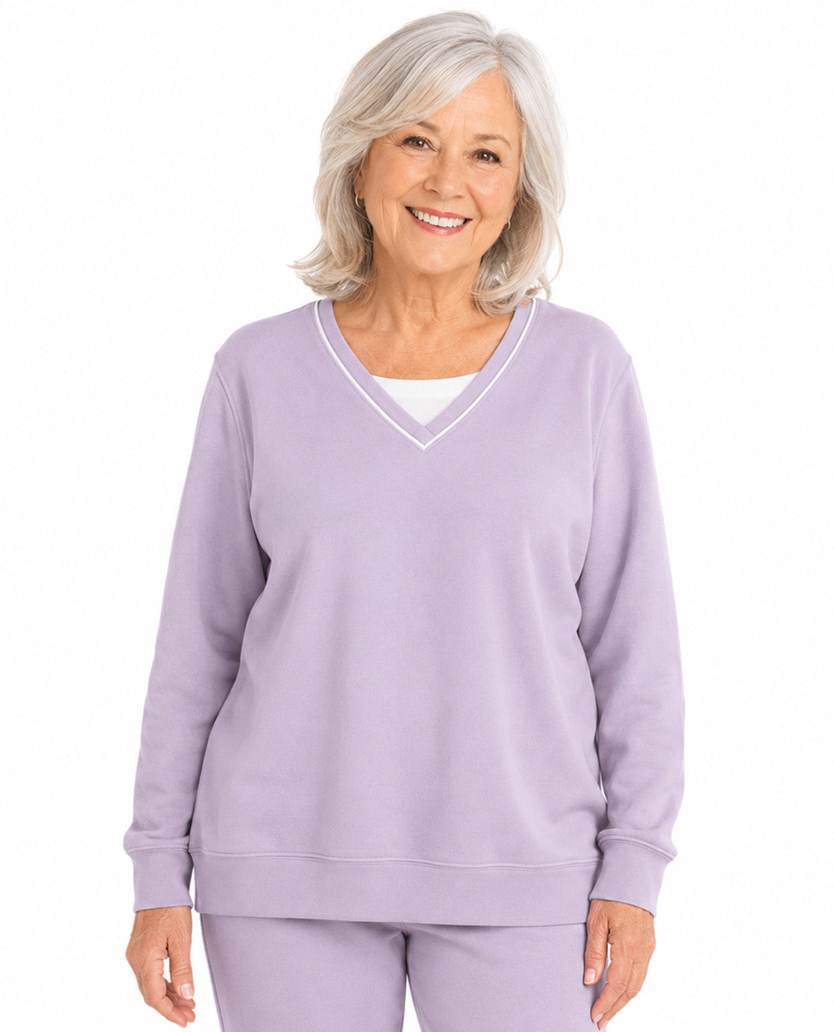 A smiling older woman with short gray hair wearing a lavender purple V-neck sweatshirt with white piping trim and matching sweatpants, shown against a plain white background.