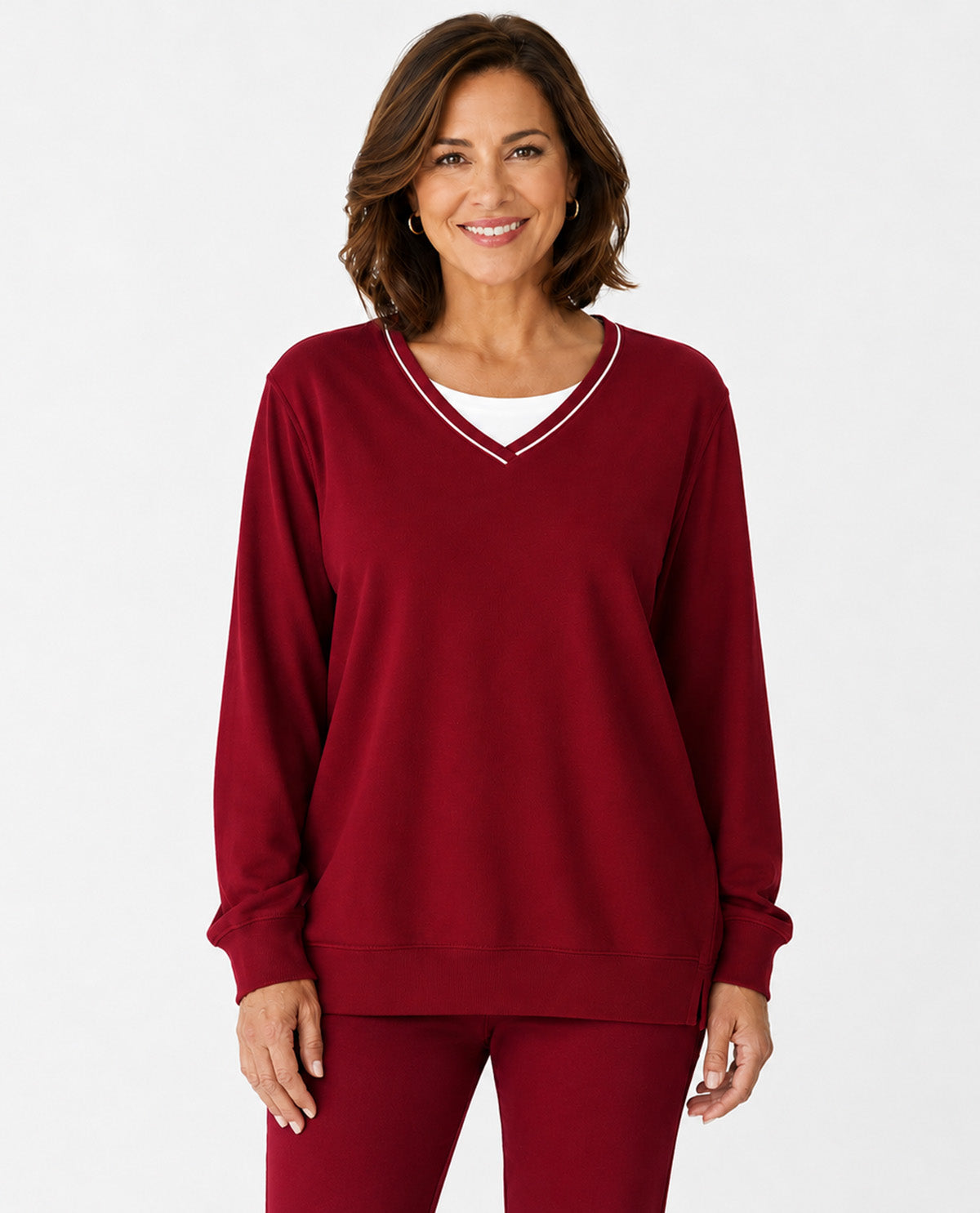 A woman modeling a long-sleeve crewneck sweatshirt in deep burgundy with a white v-neck trim, paired with matching burgundy pants, against a plain white studio background.
