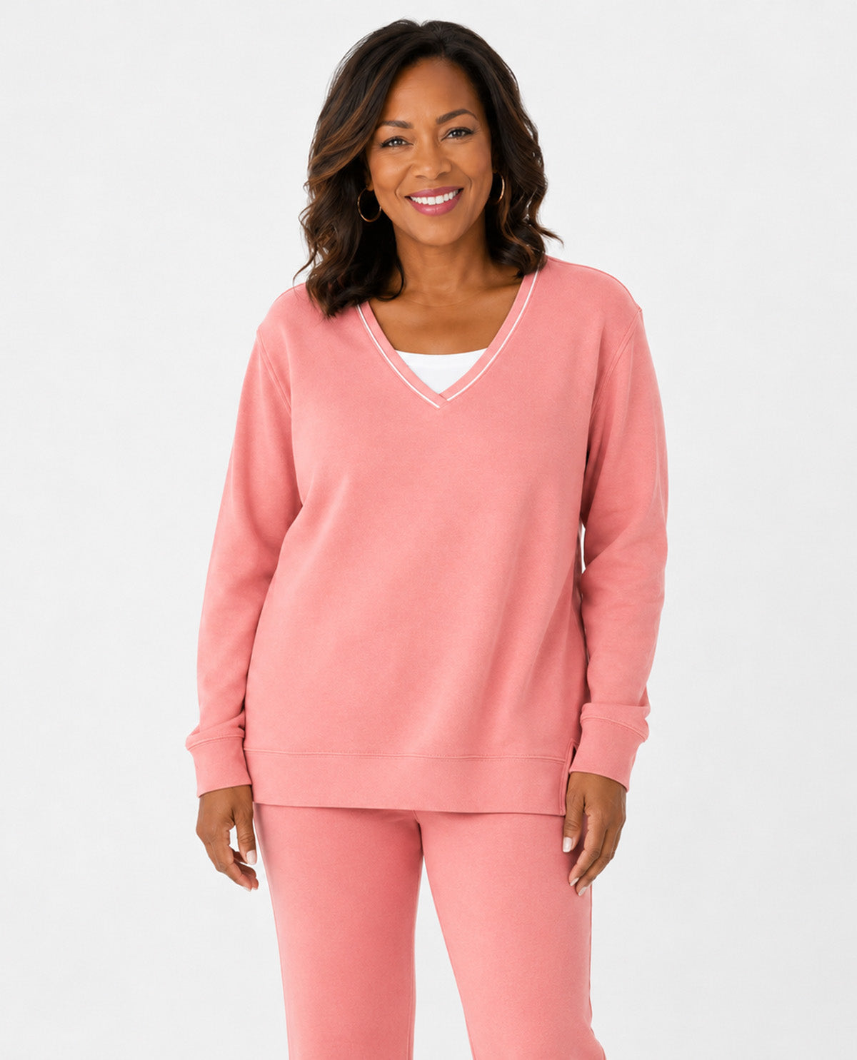 A woman modeling a matching dusty pink lounge set consisting of a V-neck long-sleeve sweatshirt and coordinating sweatpants, shot against a solid light gray background.