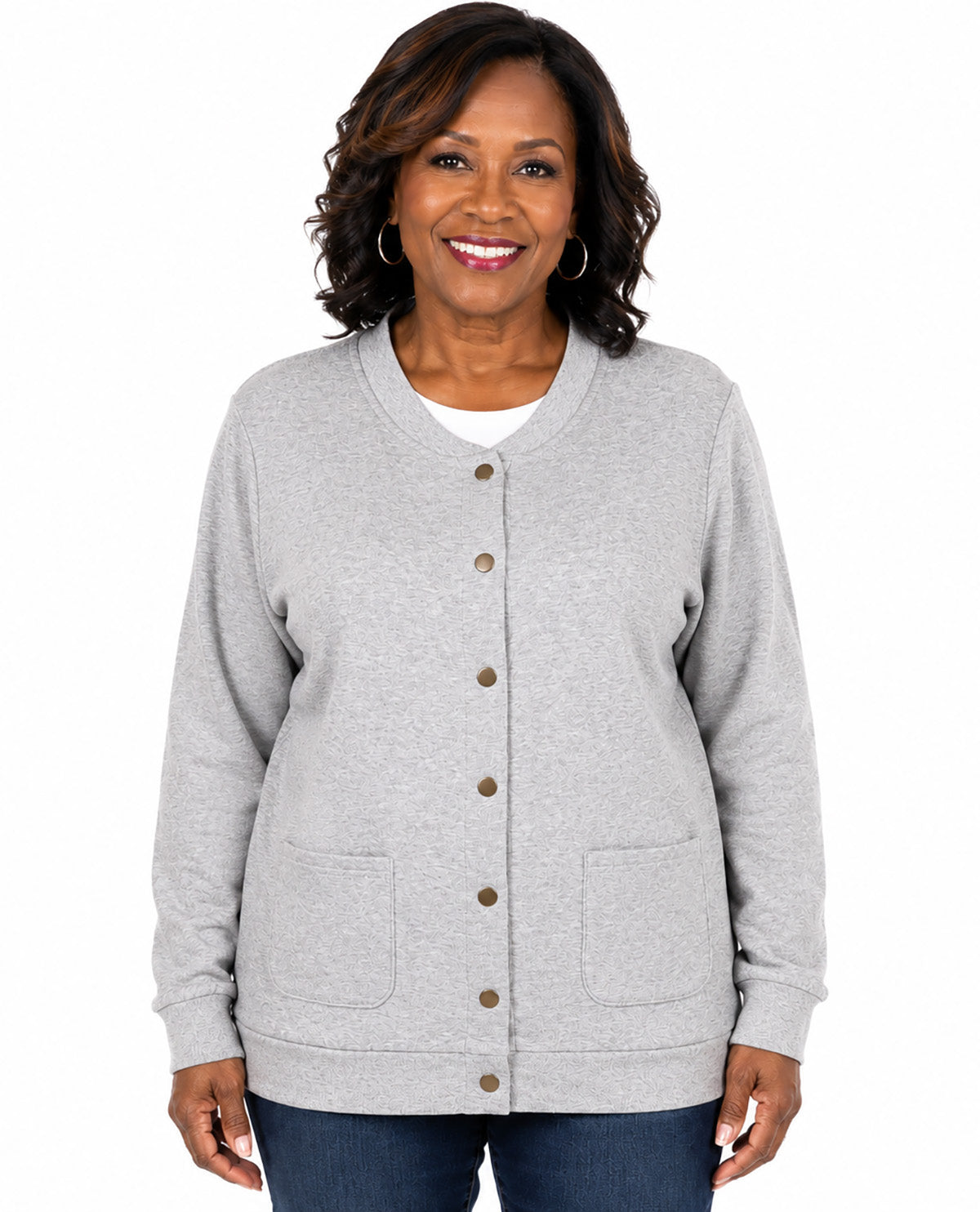 A woman wearing a light gray heather cardigan with brown buttons and front pockets, paired with a white undershirt and blue jeans, against a plain white background.