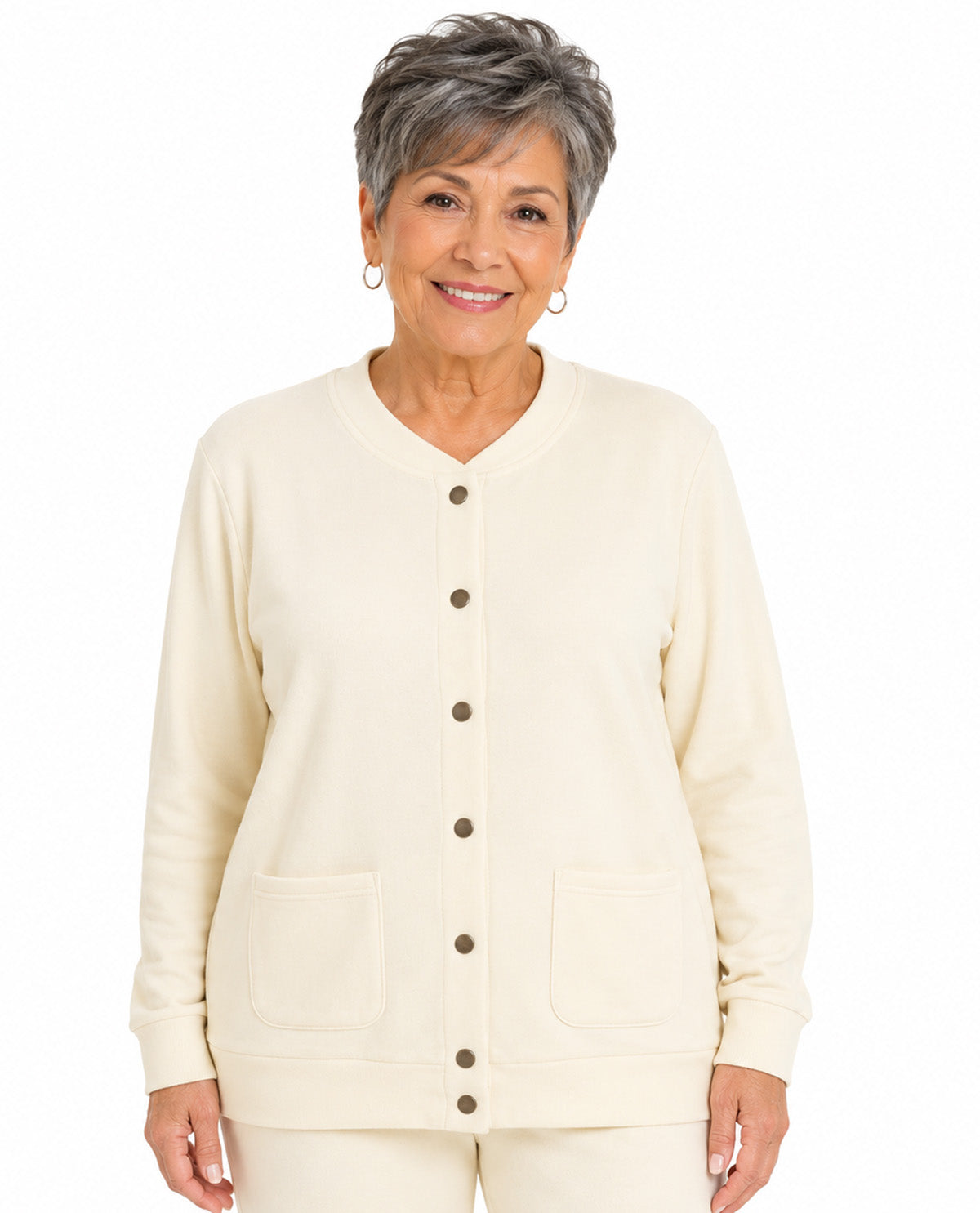 An older woman with short gray hair is wearing a cream-colored button-up cardigan with two front patch pockets, paired with matching cream pants, against a plain white background.