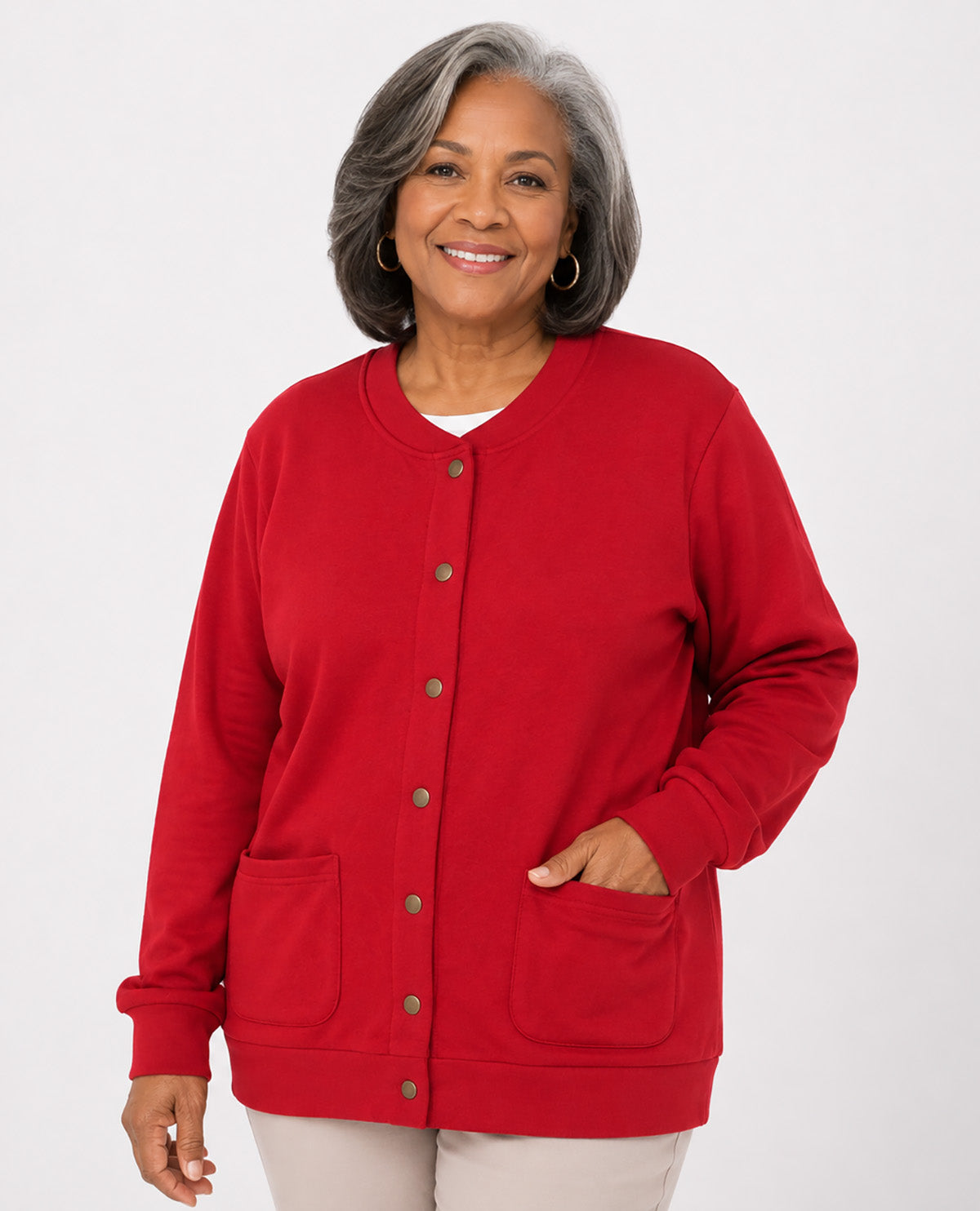 A smiling older woman with gray hair is wearing a bright red button-front cardigan with front pockets, photographed against a clean light gray studio background.