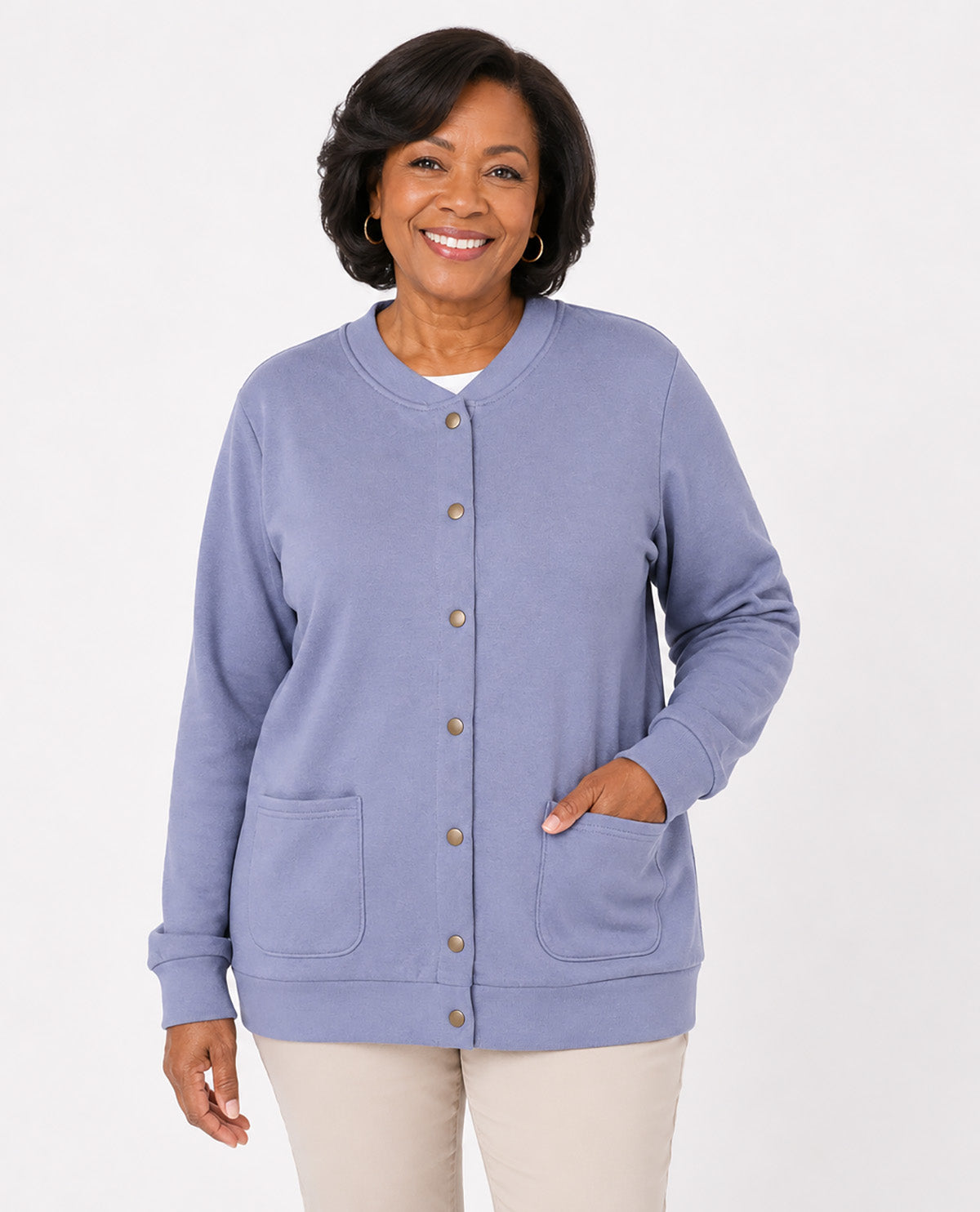 A smiling woman wearing a lavender cardigan sweater with front buttons and patch pockets, paired with light beige pants, against a plain white studio background.