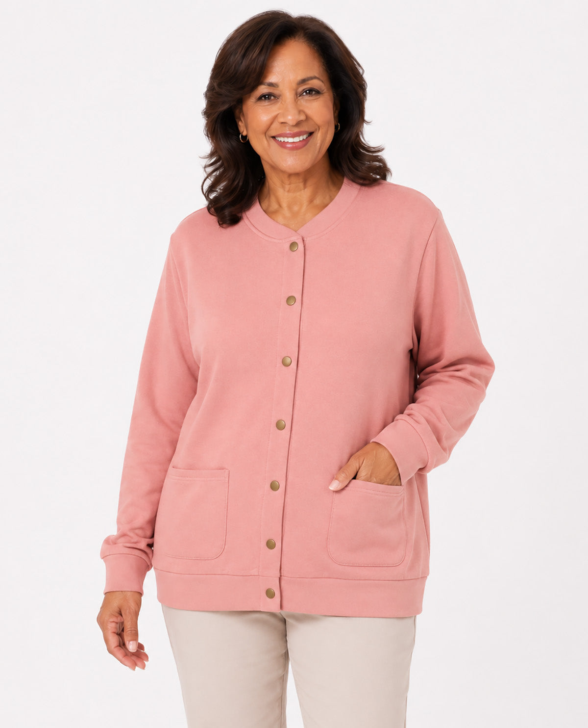 A smiling woman wearing a dusty pink button-front cardigan with front pockets and light beige pants, photographed against a clean white studio background.