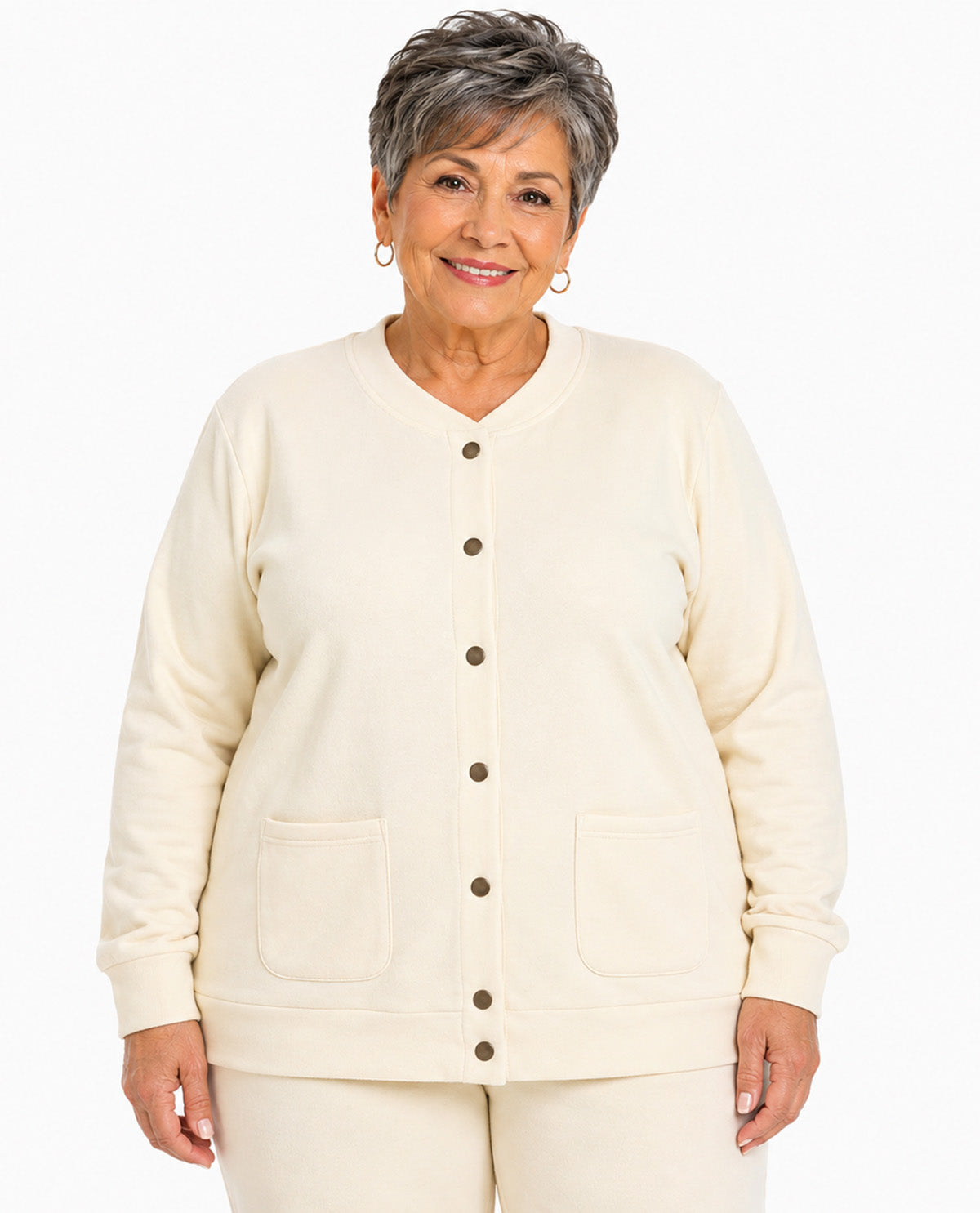 A smiling older woman wearing a cream-colored button-front cardigan with two front patch pockets and matching cream pants, photographed against a plain white studio background.