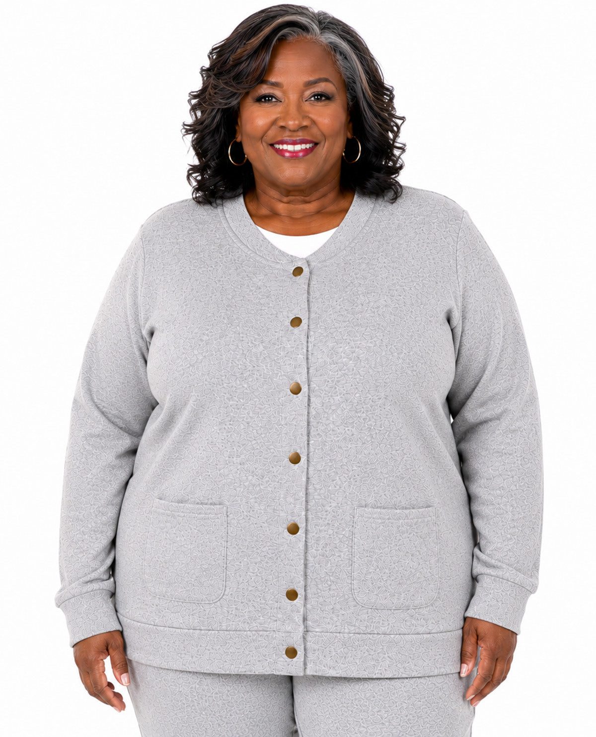 A smiling woman with dark curly hair models a light gray heather cardigan sweater with brown buttons, featuring a V-neck, long sleeves, and front patch pockets, paired with matching gray pants against a plain white background.