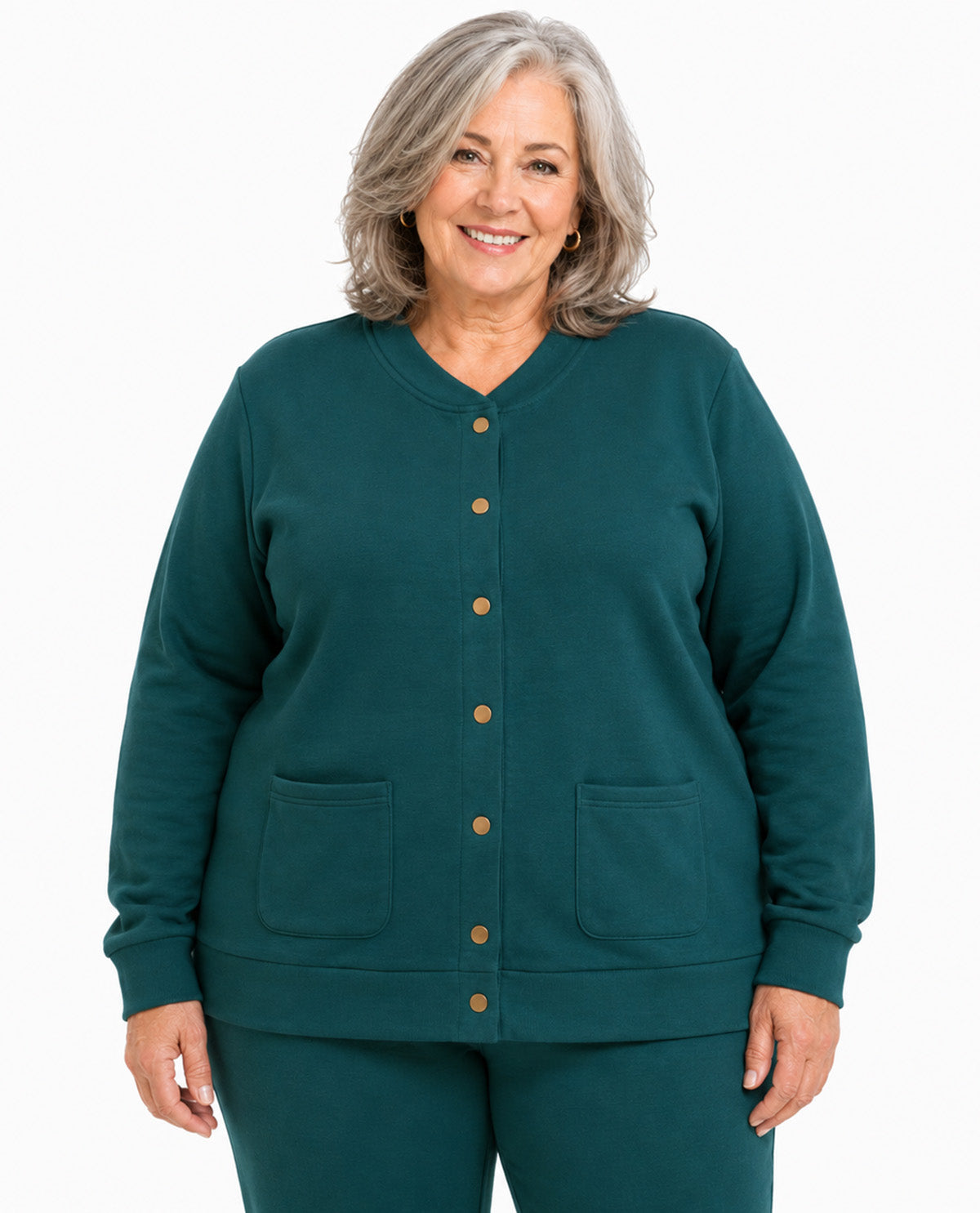 A smiling older woman with gray hair stands against a plain white background wearing a dark teal green button-front cardigan with two front patch pockets and matching green pants.