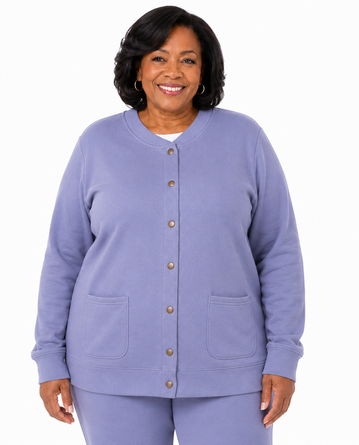A smiling woman wearing a lavender cardigan-style top with front buttons and two front patch pockets, paired with matching pants, against a plain white studio background.