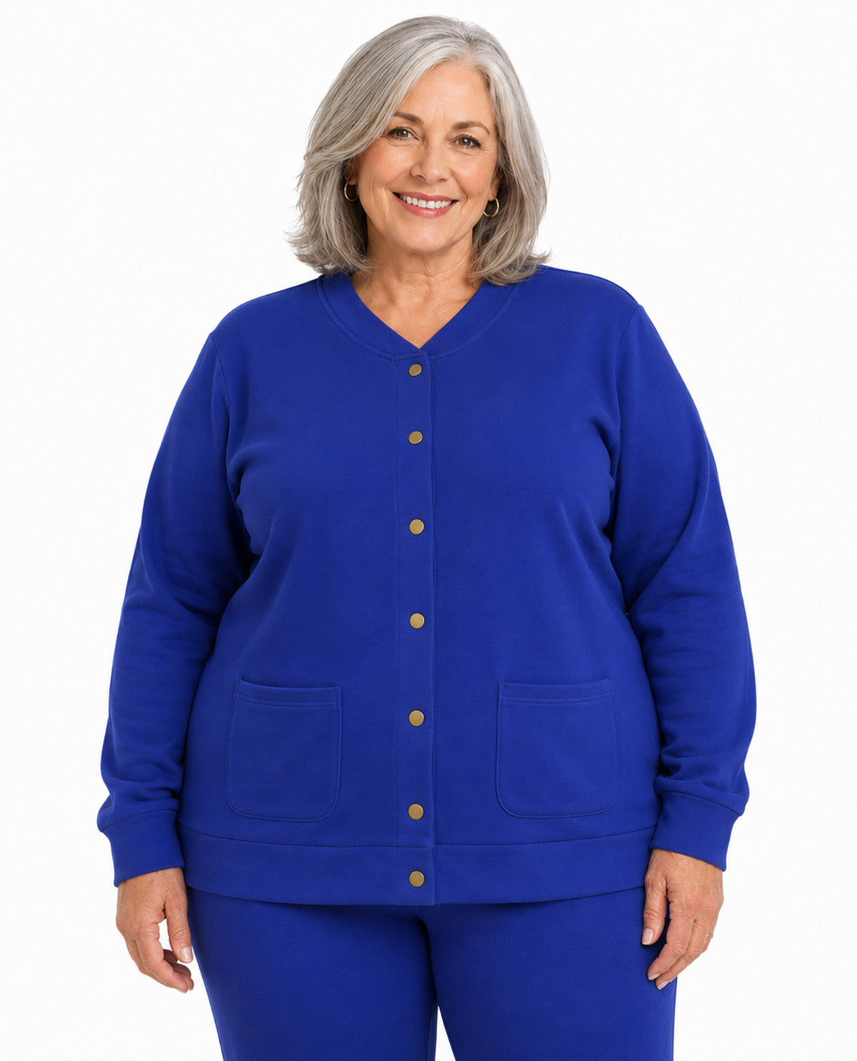 A smiling older woman with gray hair stands against a plain white background wearing a bright royal blue button-front cardigan-style top with two front patch pockets and matching blue pants.