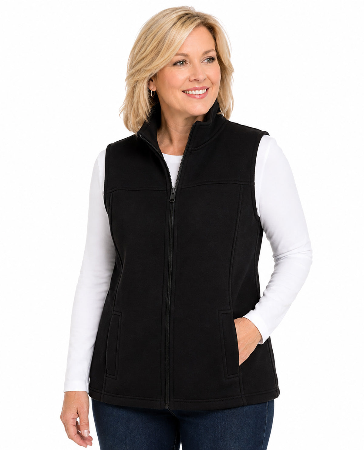 A woman wearing a black zip-up fleece vest over a white long-sleeve shirt and dark blue jeans, photographed against a plain white studio background.