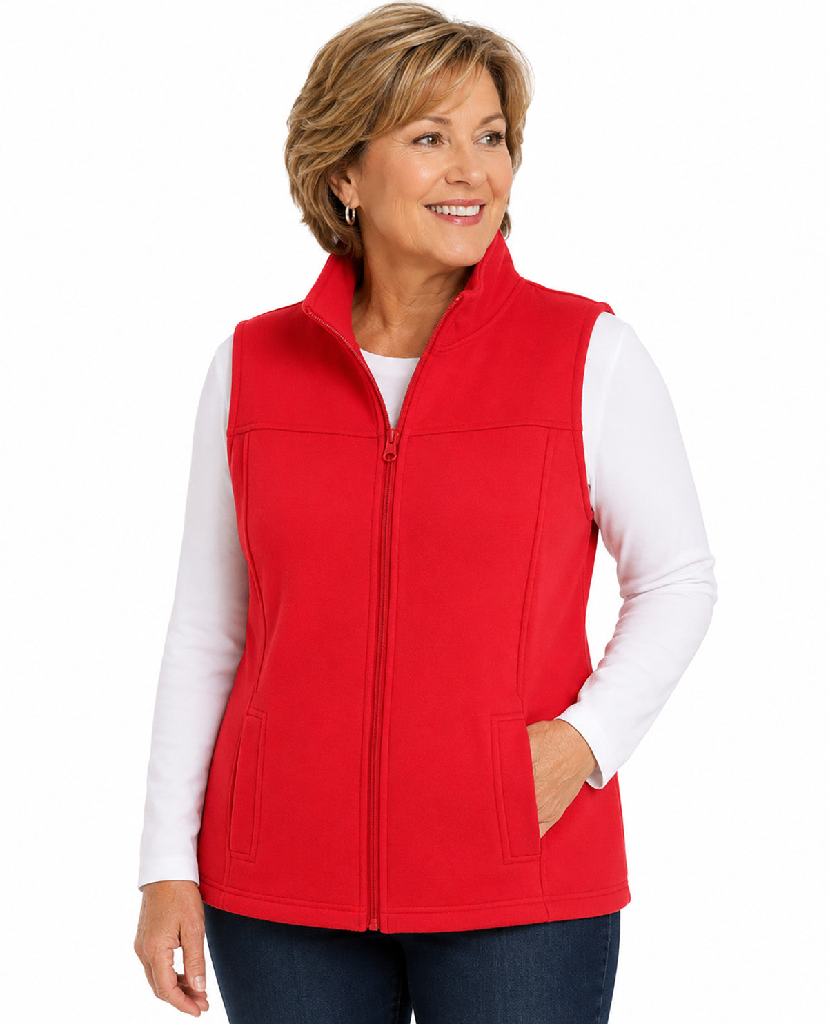 A smiling woman wearing a bright red zip-front fleece vest over a white long-sleeve top and dark blue jeans, photographed against a plain white studio background.