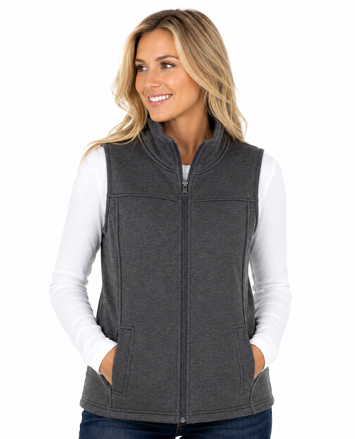 A woman wearing a dark gray zip-up fleece vest over a white long-sleeve shirt and blue jeans, photographed against a plain white studio background.
