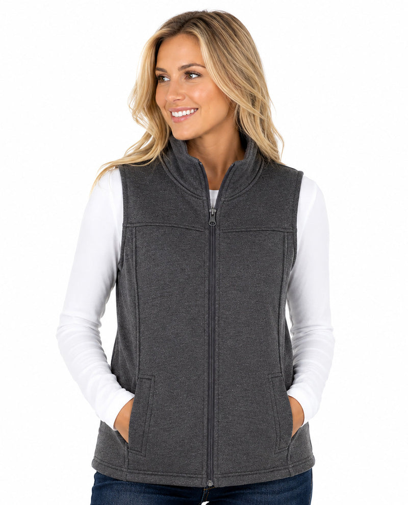 A woman wearing a dark gray zip-up fleece vest over a white long-sleeve shirt and blue jeans, photographed against a plain white studio background.