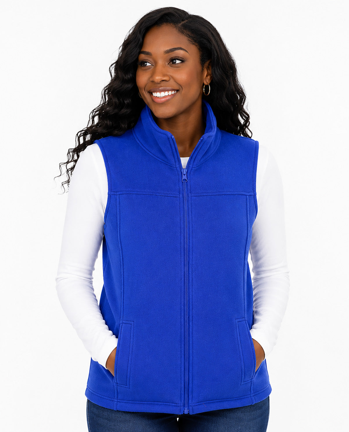 A woman wearing a bright royal blue zip-up fleece vest over a white long-sleeve shirt and dark blue jeans, photographed against a clean white studio background.