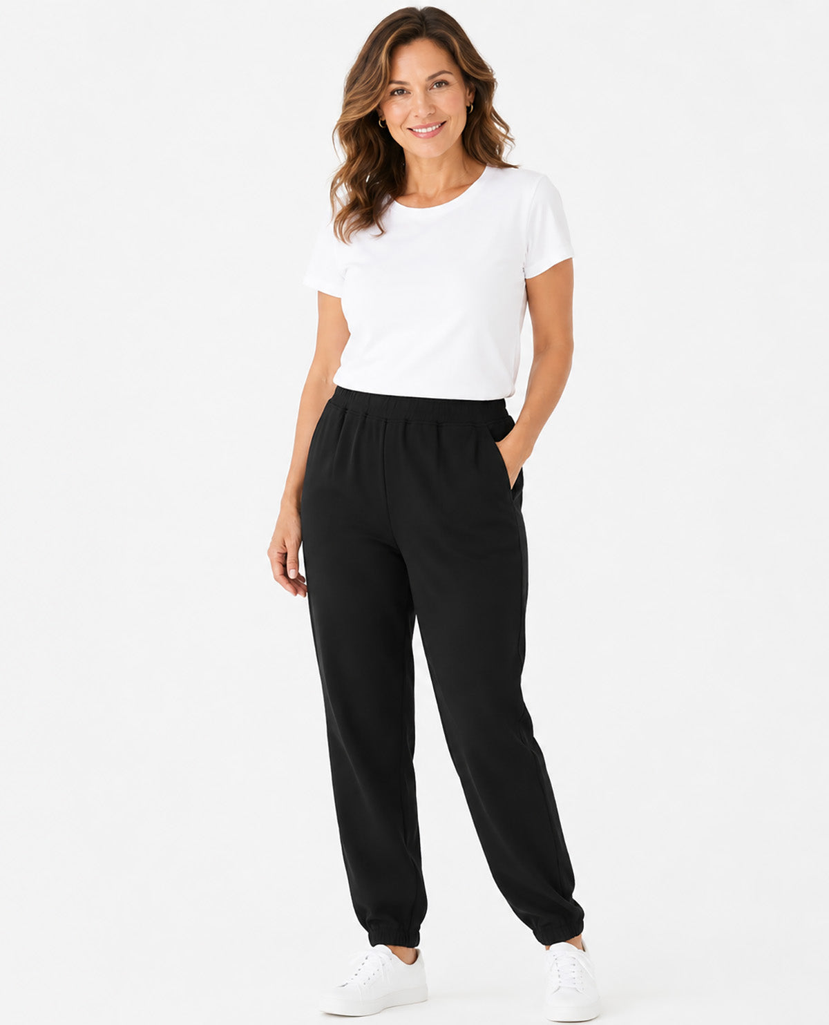 A woman modeling black jogger-style pants with a white t-shirt and white sneakers against a plain white studio background.