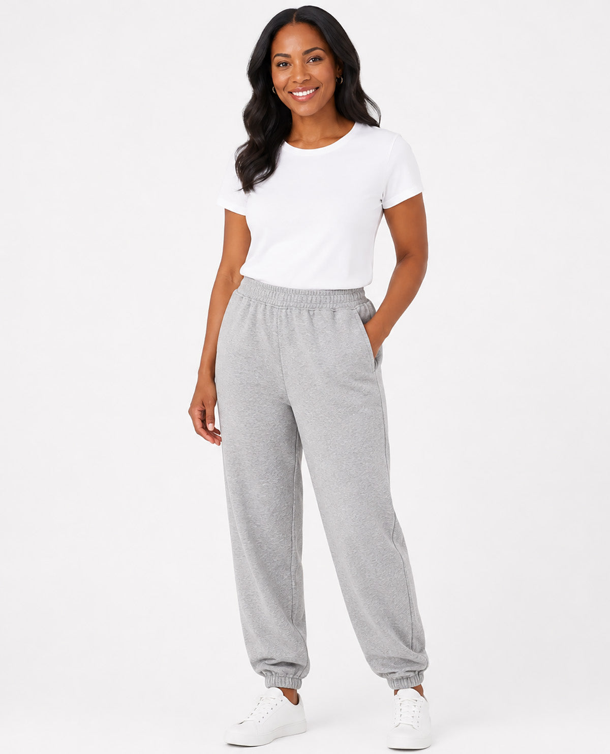 A woman modeling light gray heather sweatpants with an elastic waistband and cuffs, paired with a white t-shirt and white sneakers, against a plain white studio background.