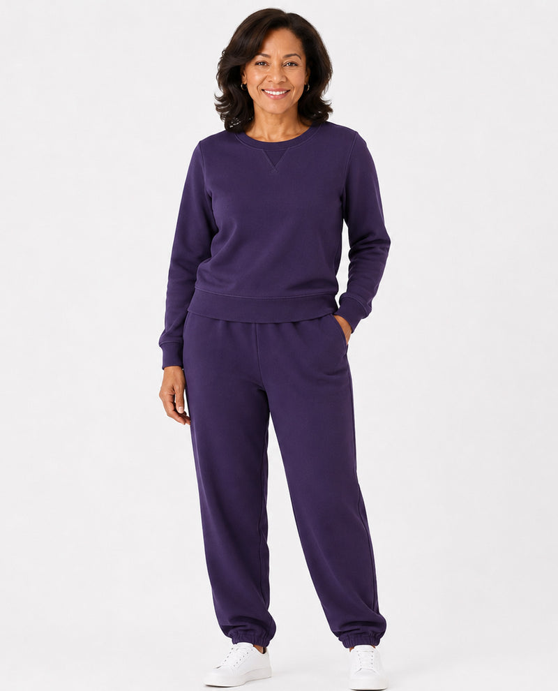 A woman modeling a matching purple sweatshirt and jogger pants set against a plain white studio background.
