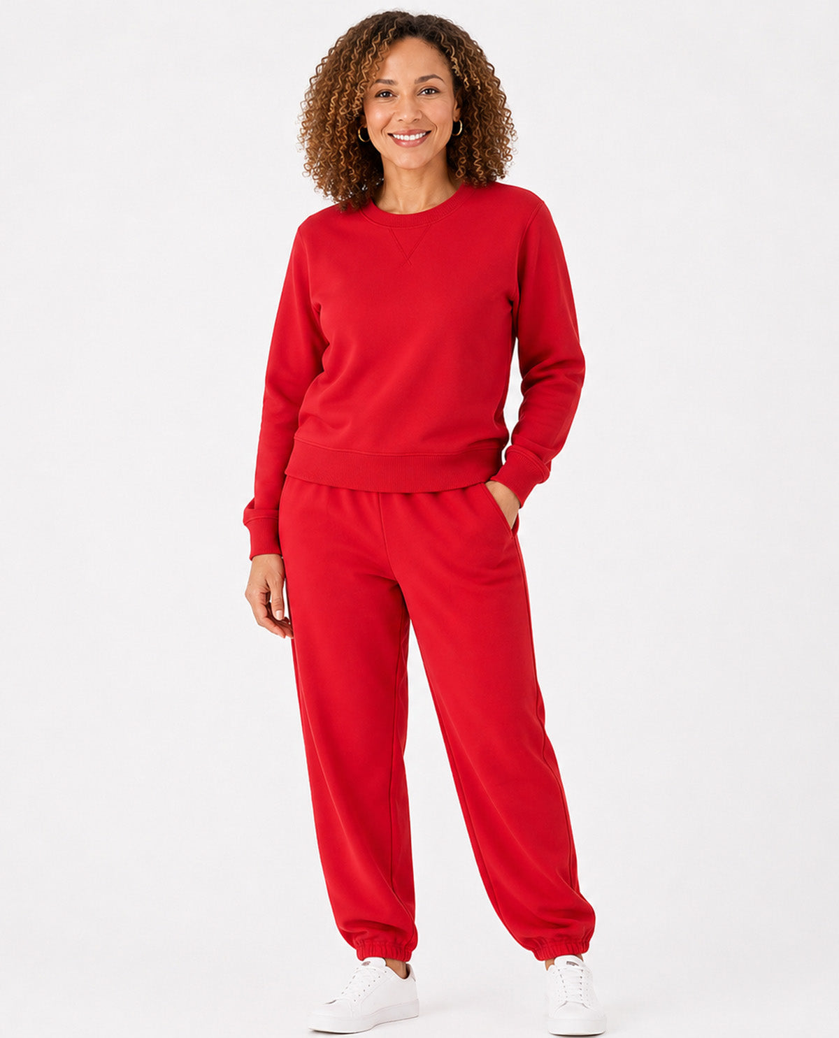 A woman modeling a matching red sweatshirt and jogger pants set, paired with white sneakers, against a plain white studio background.