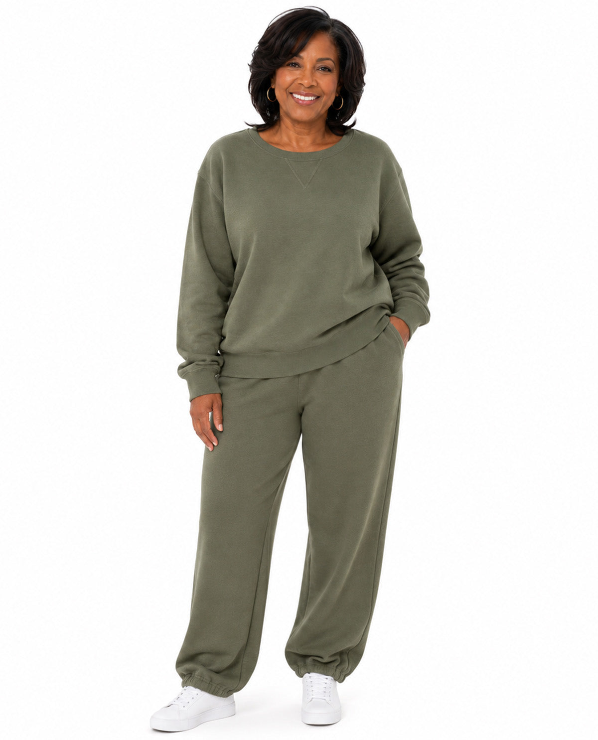A woman modeling a matching two-piece lounge set in olive green, featuring a long-sleeve crewneck sweatshirt and matching jogger pants, paired with white sneakers against a plain white background.