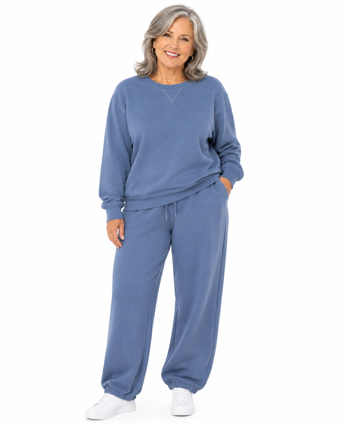 A woman modeling a matching dusty blue sweatshirt and sweatpants lounge set against a plain white background.