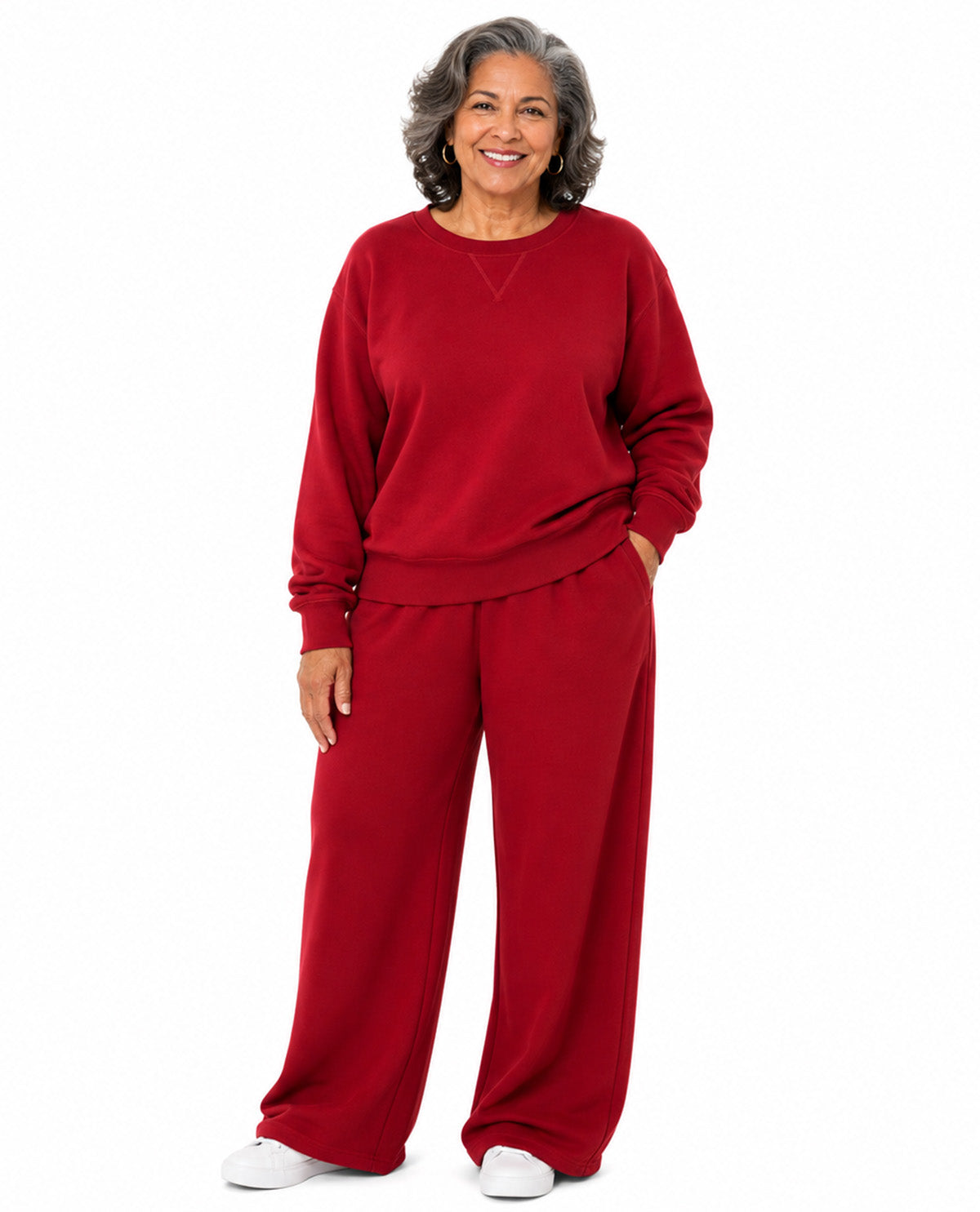 A smiling older woman stands against a plain white background wearing a matching red lounge set consisting of a long-sleeve sweatshirt and wide-leg pants.