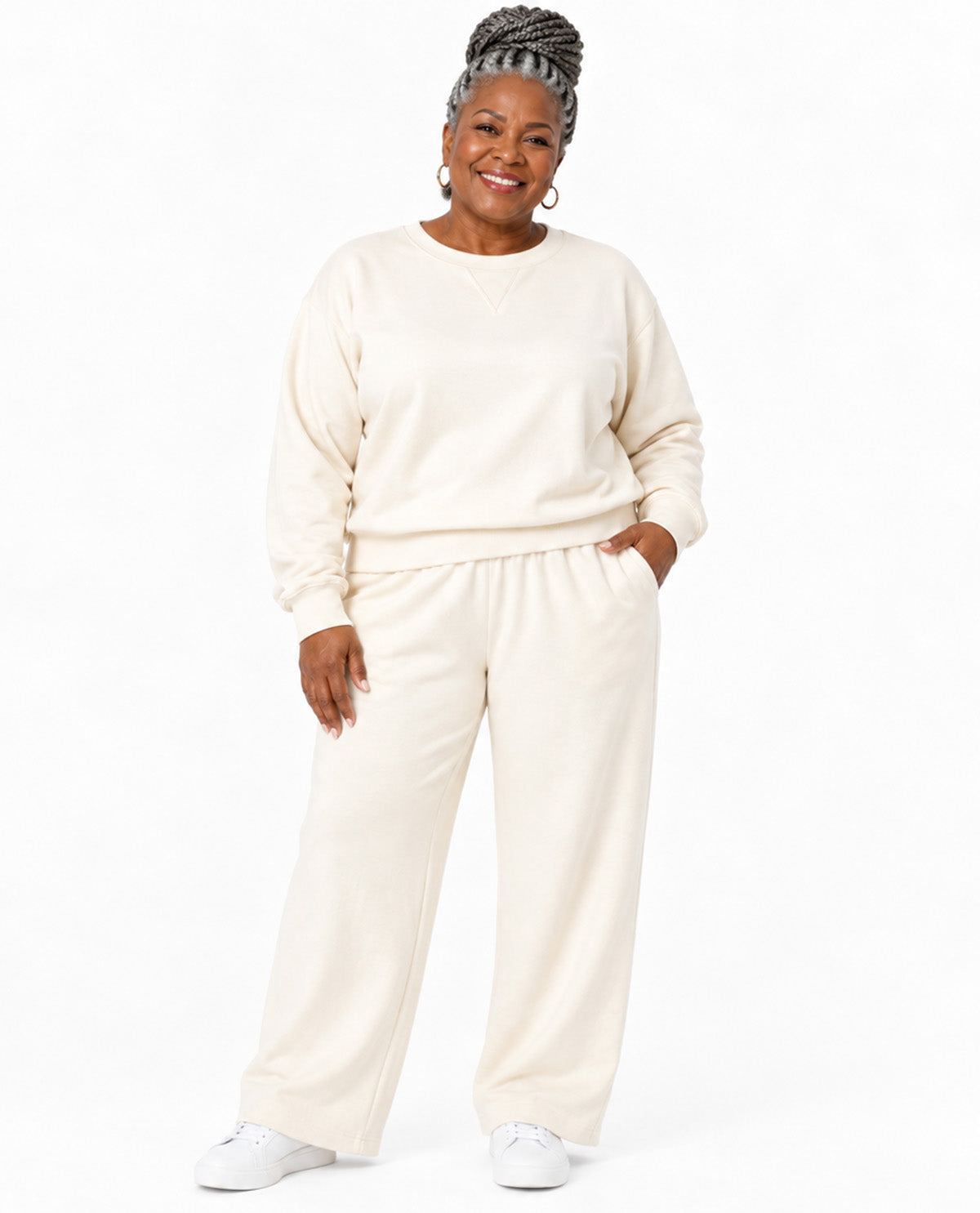 A woman modeling a matching cream sweatshirt and wide-leg sweatpants lounge set against a plain white studio background.